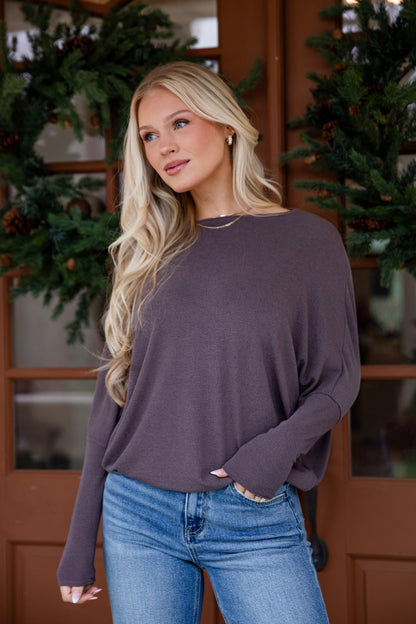 Woman wearing a purple sweater and blue jeans standing in front of a wooden door with greenery.