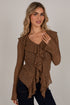 A woman wearing a brown textured knit long-sleeve top with ruffle details and dark jeans, posing against a light gray studio background.