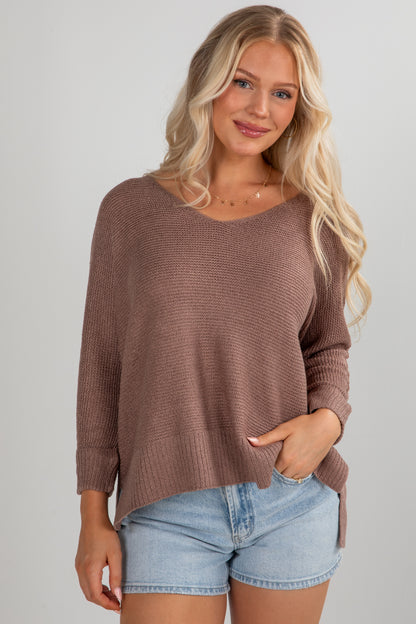 Woman wearing a brown sweater and denim shorts on a plain background