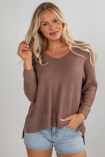 Woman wearing a brown sweater and denim shorts against a plain background