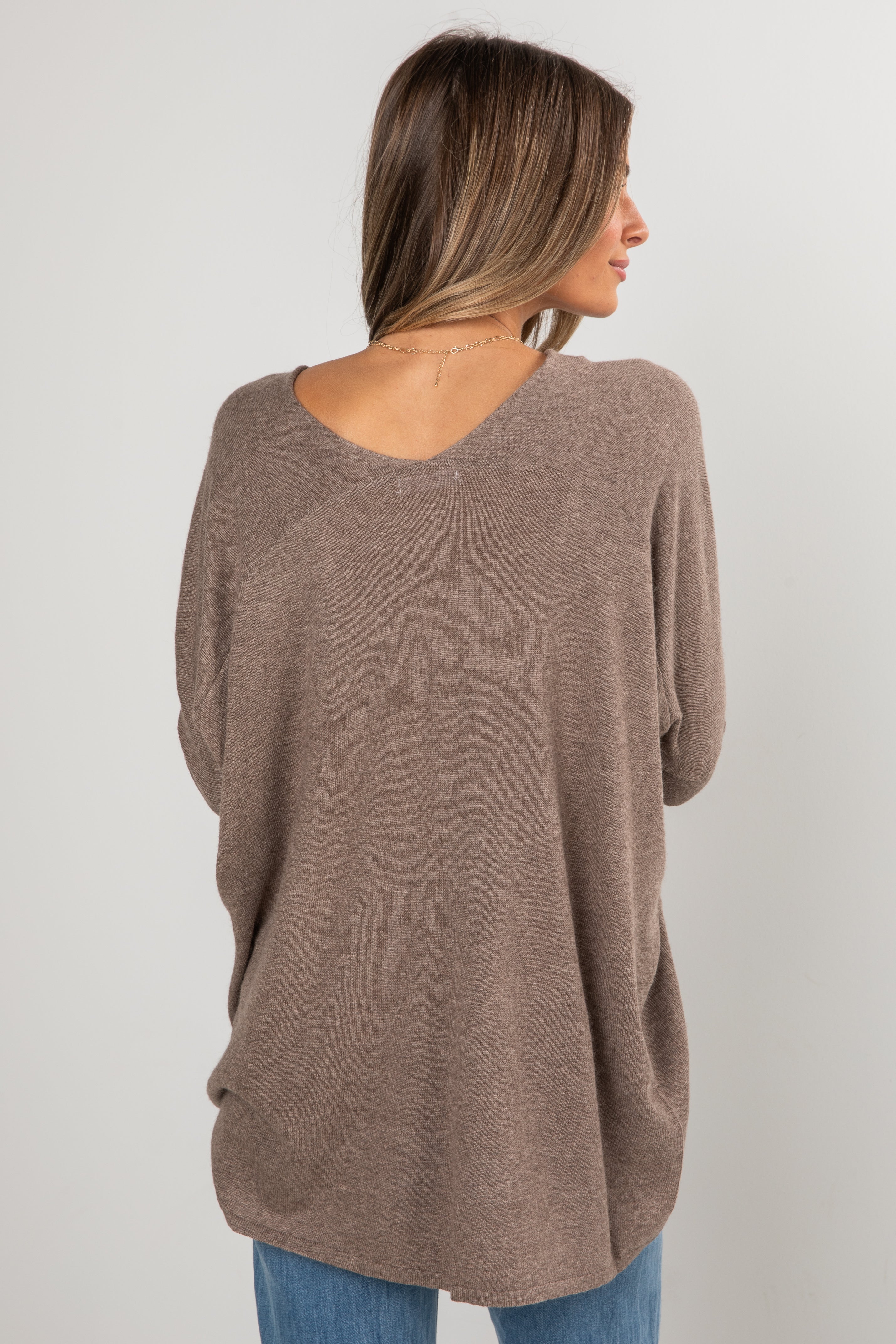 Woman wearing a brown sweater from behind on a plain background