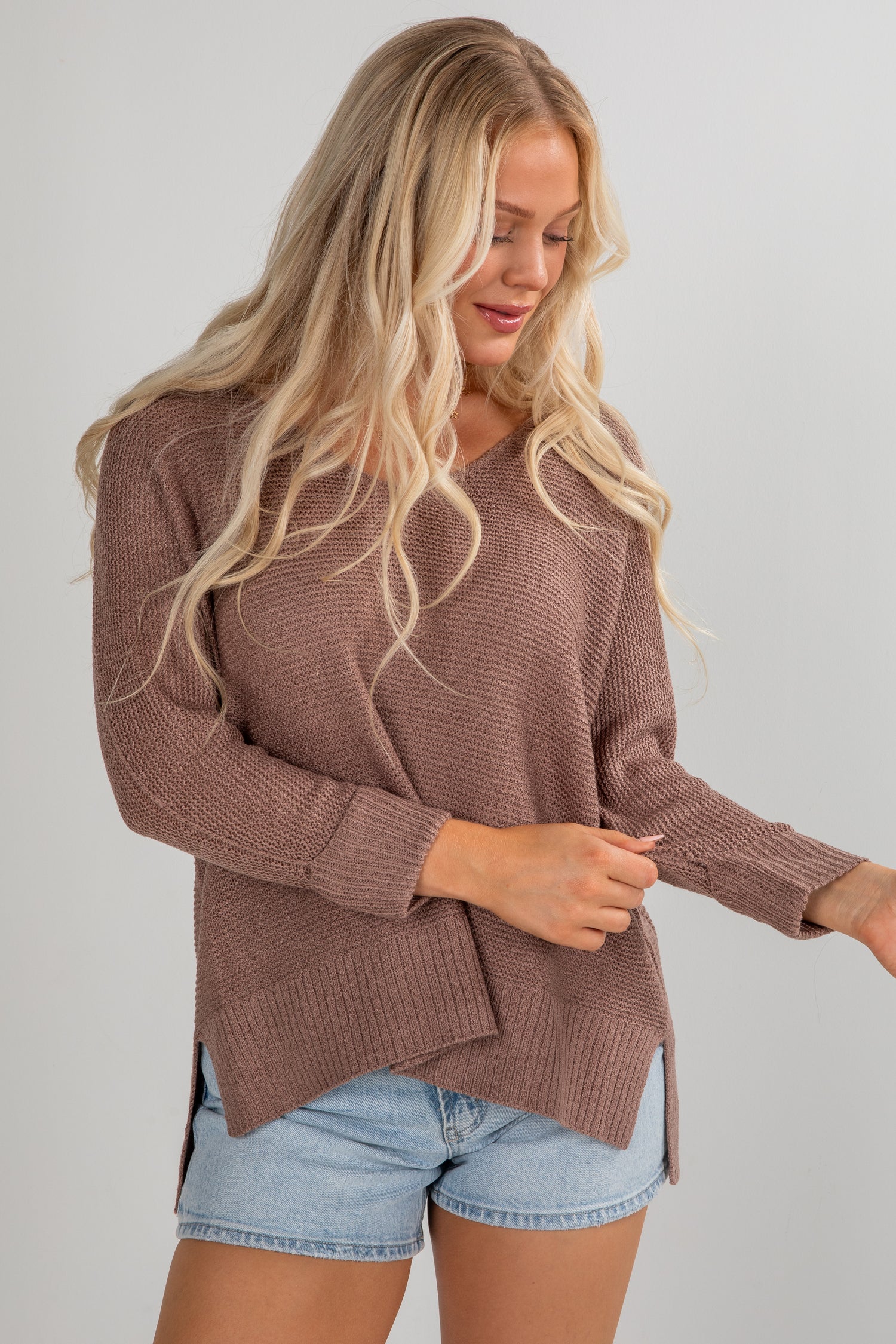 Woman wearing a brown sweater and denim shorts on a plain background