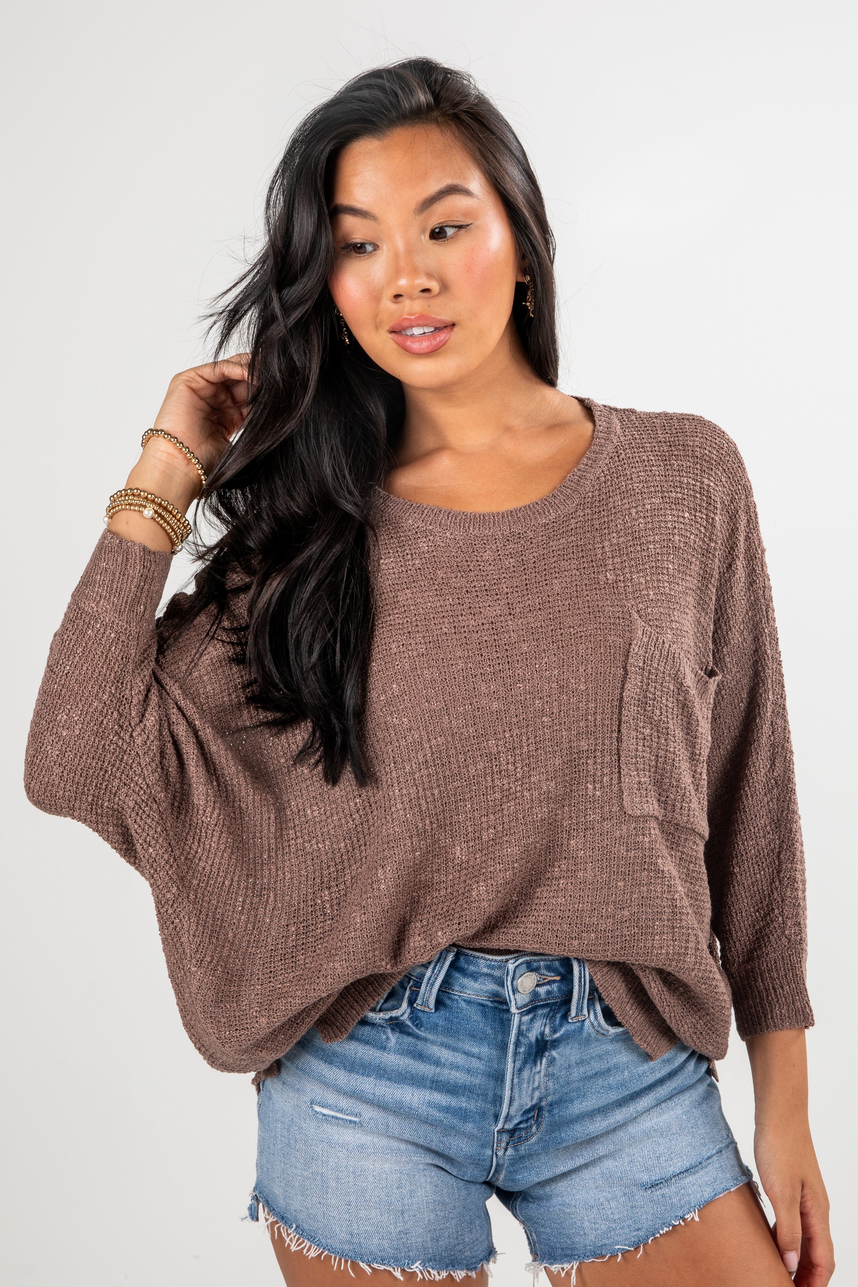 Woman wearing a brown sweater and denim shorts on a white background