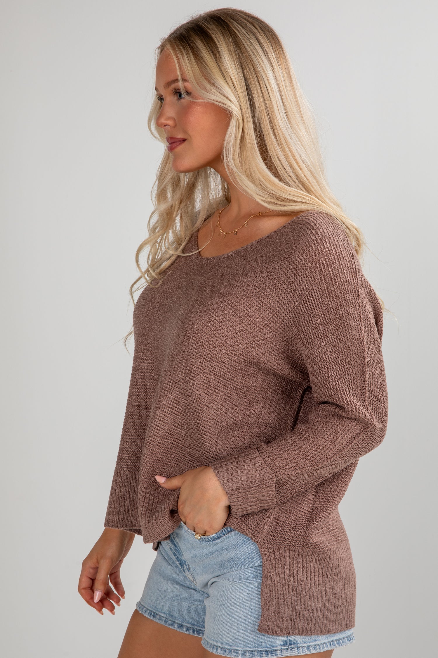 Woman wearing a brown sweater and denim shorts on a plain background