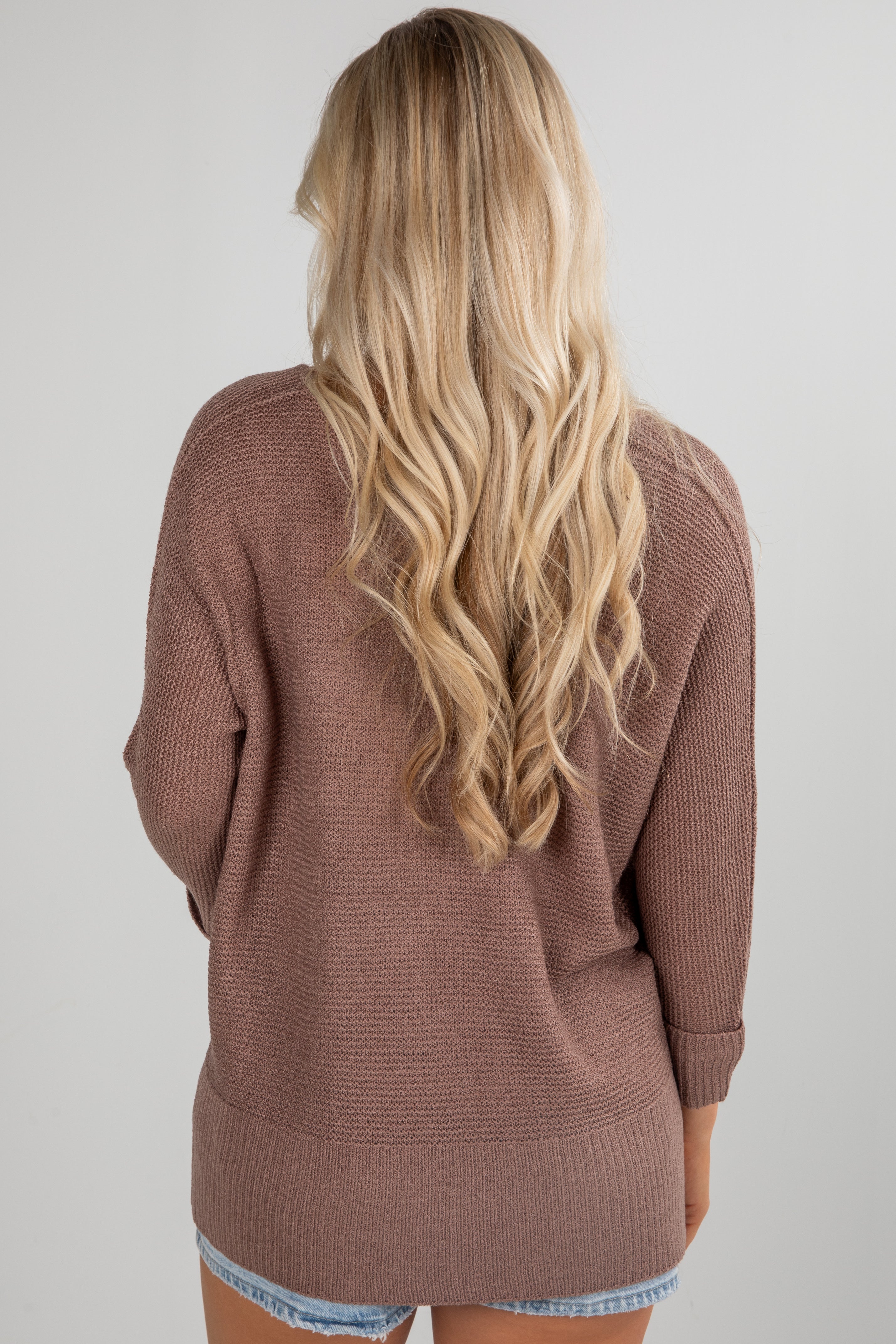 Person wearing a brown cardigan with long blonde hair on a plain background