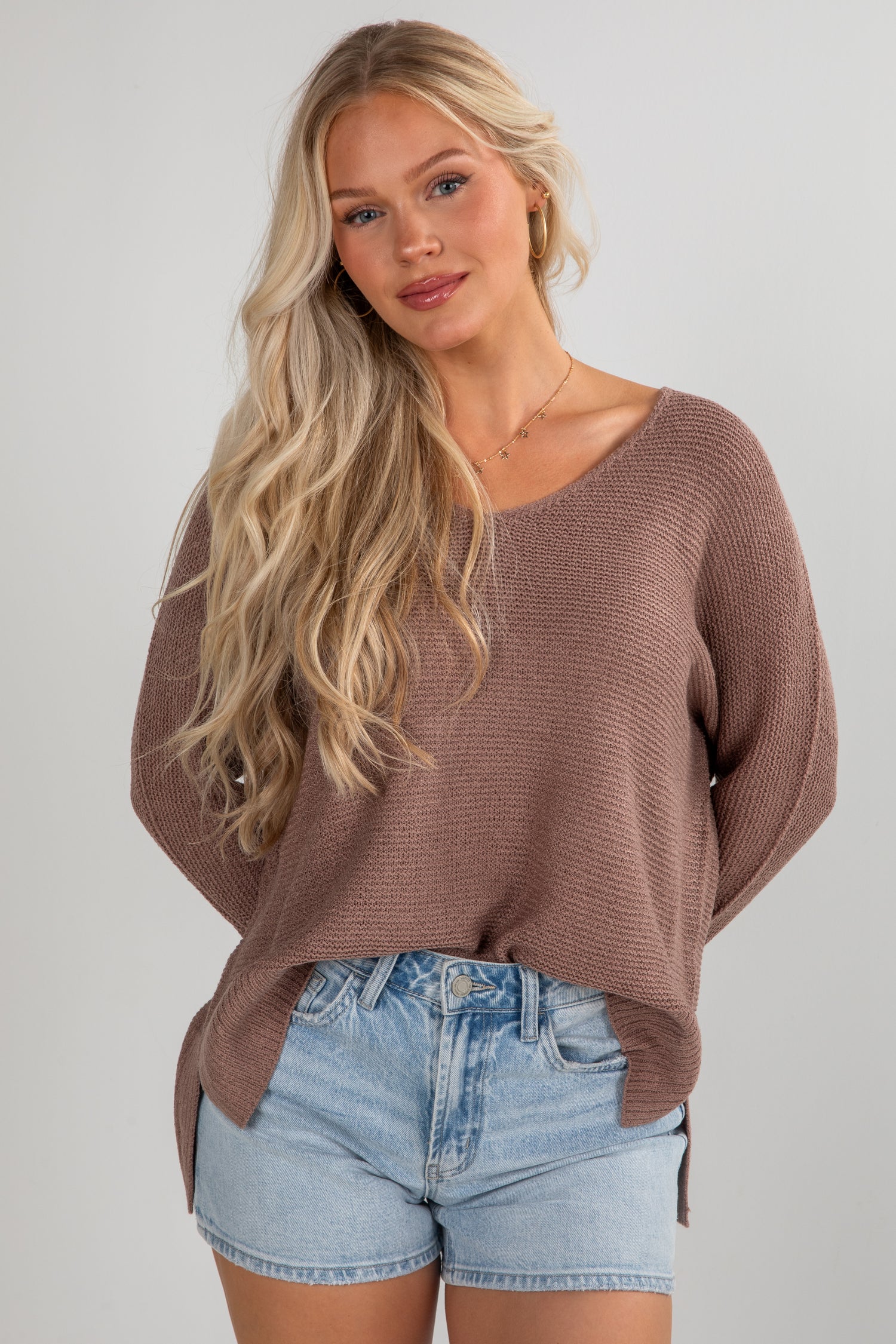 Woman wearing a brown sweater and denim shorts on a plain background