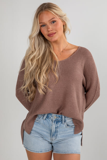 Woman wearing a brown sweater and denim shorts on a plain background