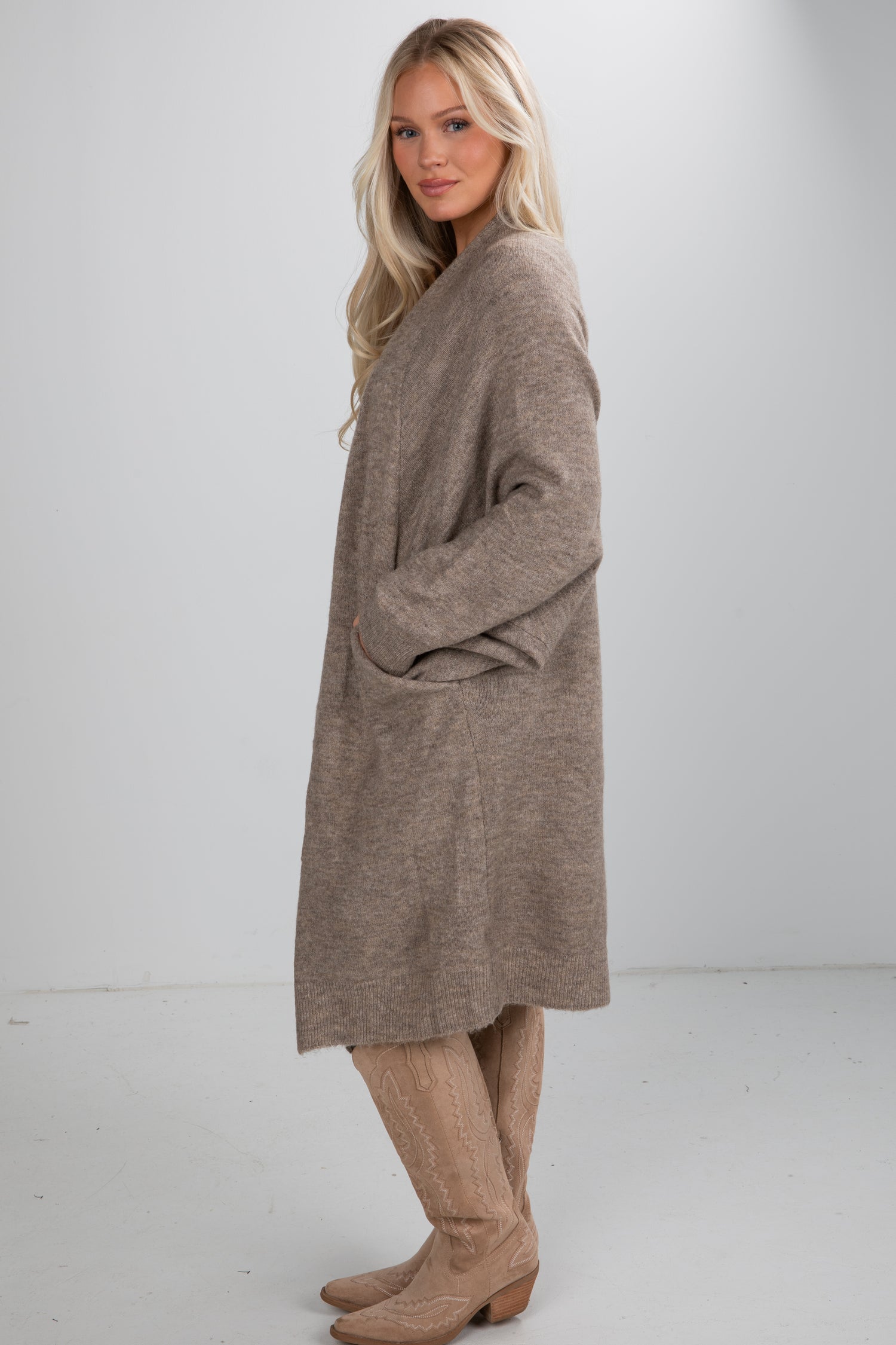 Woman wearing a long brown sweater dress with beige boots on a white background