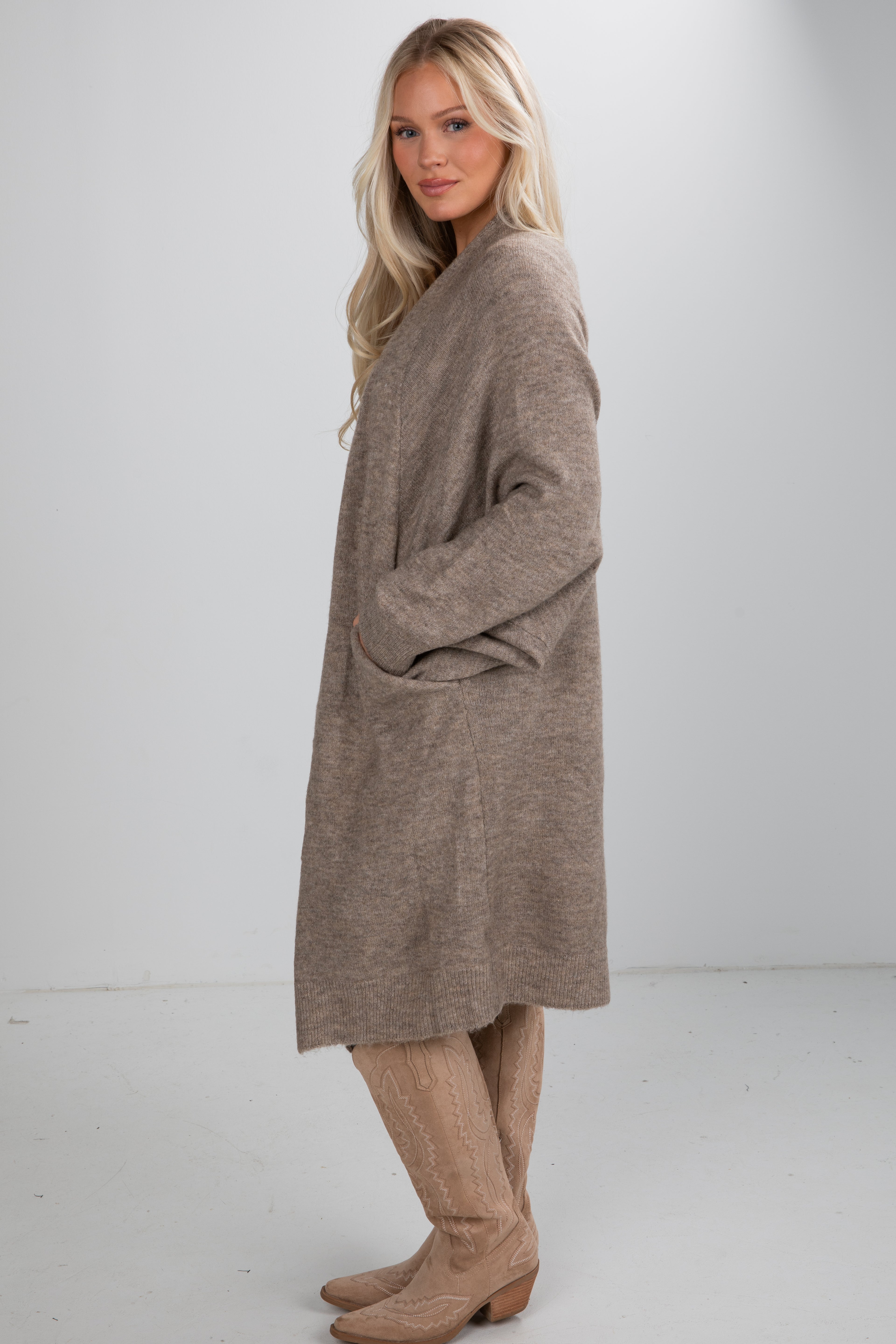 Woman wearing a long brown sweater dress with beige boots on a white background