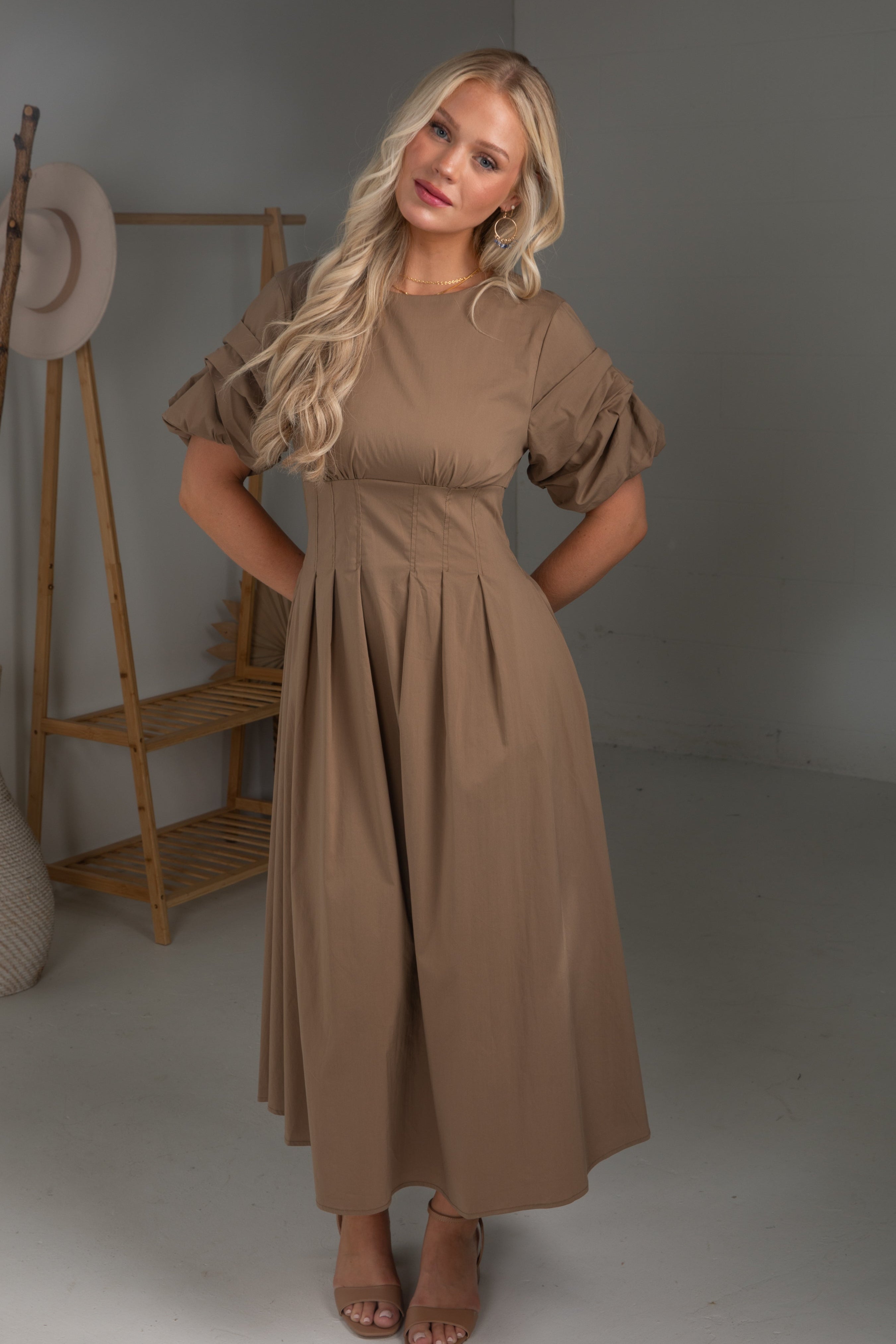 Woman wearing a brown dress standing in a studio setting with a gray background