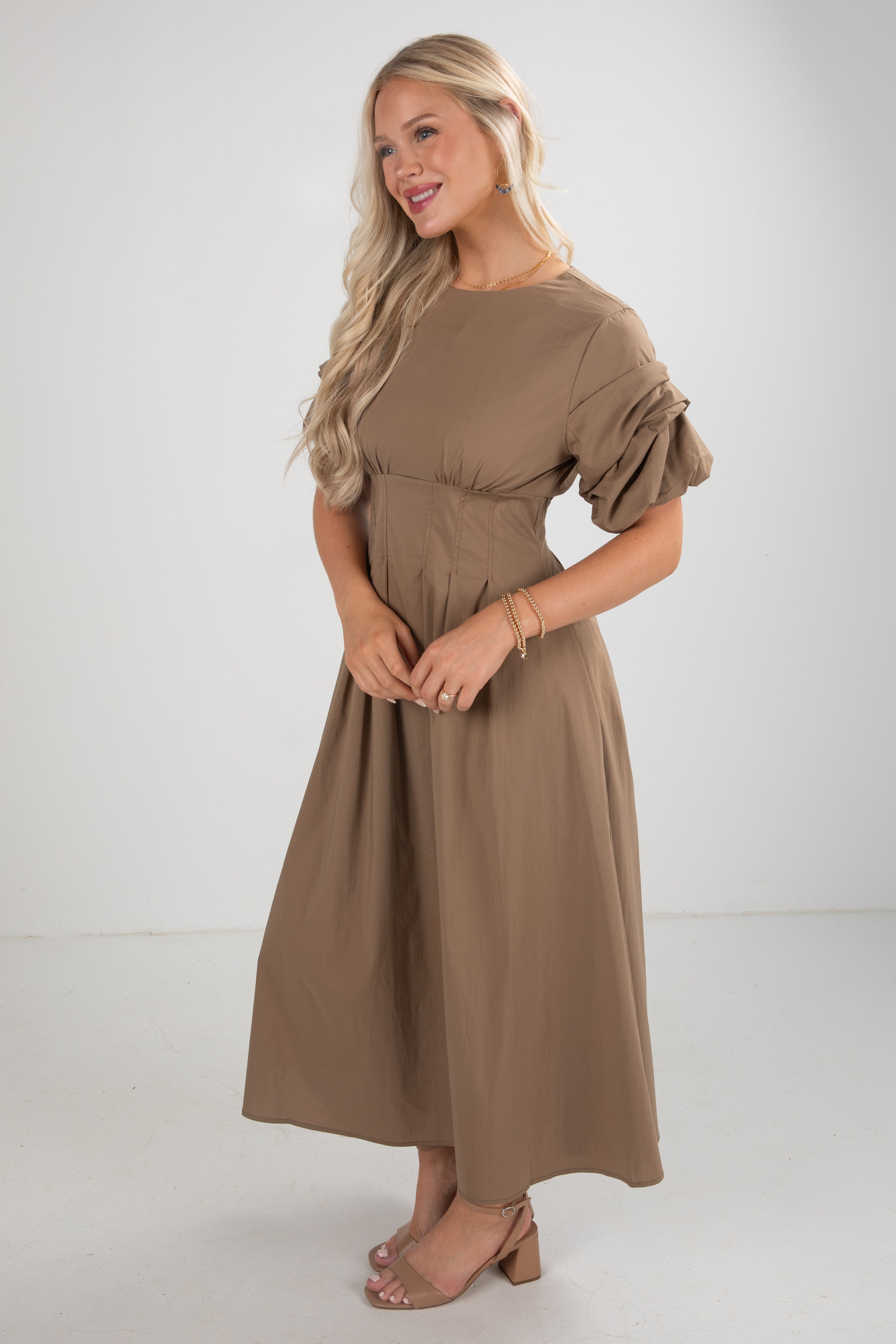 Woman wearing a brown dress with puff sleeves on a white background