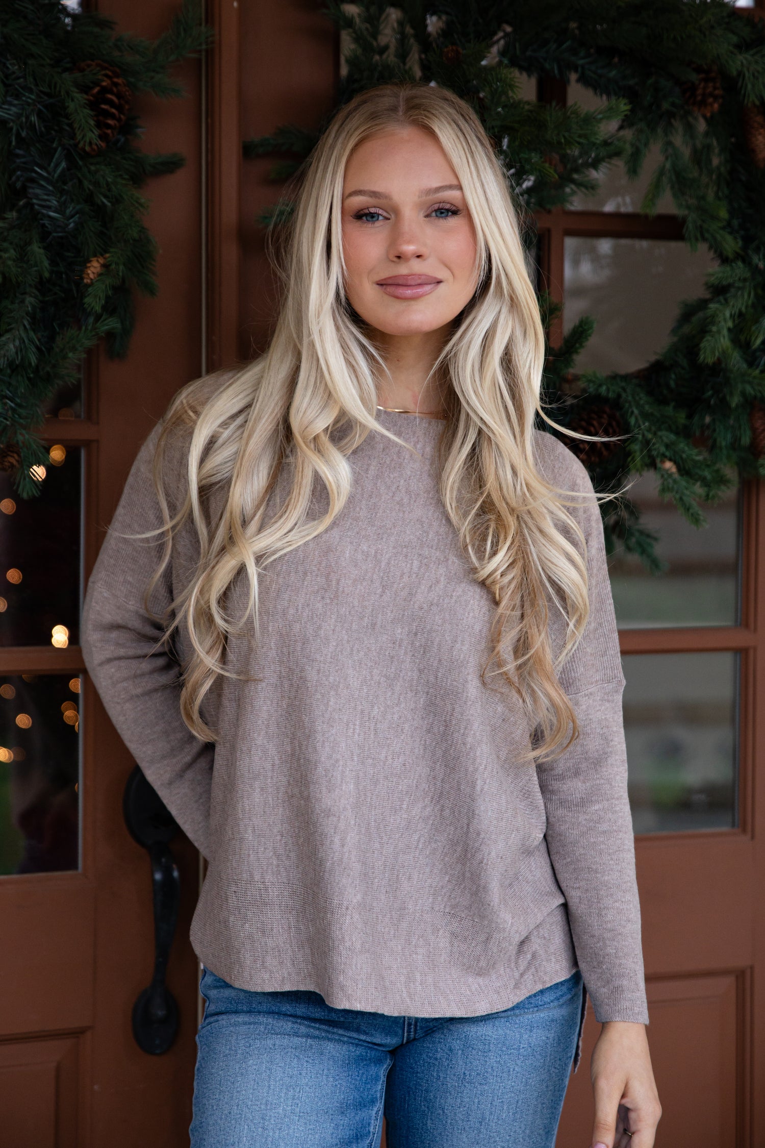 Woman wearing a beige sweater and blue jeans standing in front of a decorated door.