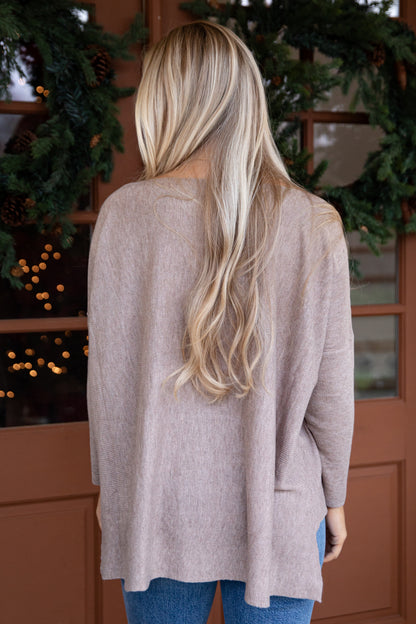 Person wearing a beige cardigan in front of a decorated door with greenery and lights.