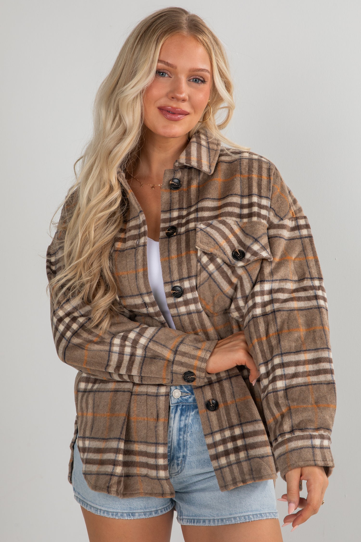 Woman wearing a plaid jacket and denim shorts on a plain background