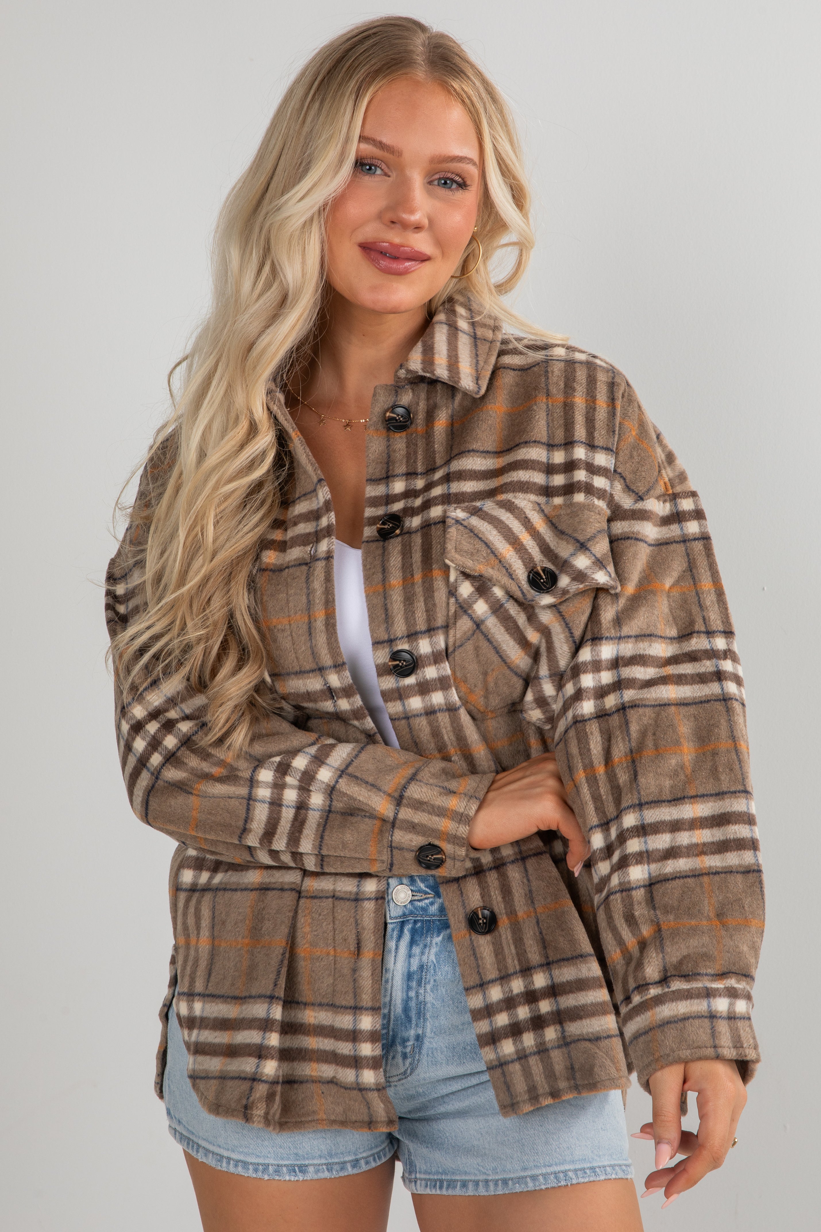 Woman wearing a plaid jacket and denim shorts on a plain background
