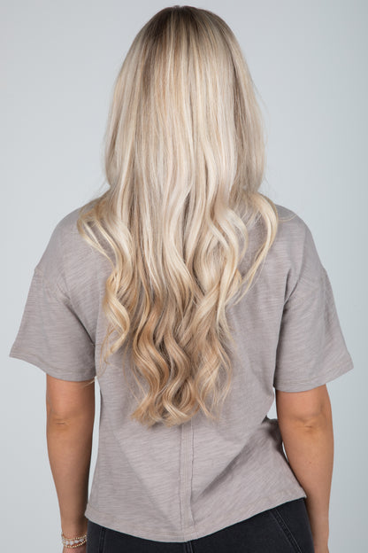 Person with long, wavy blonde hair wearing a gray shirt on a plain background