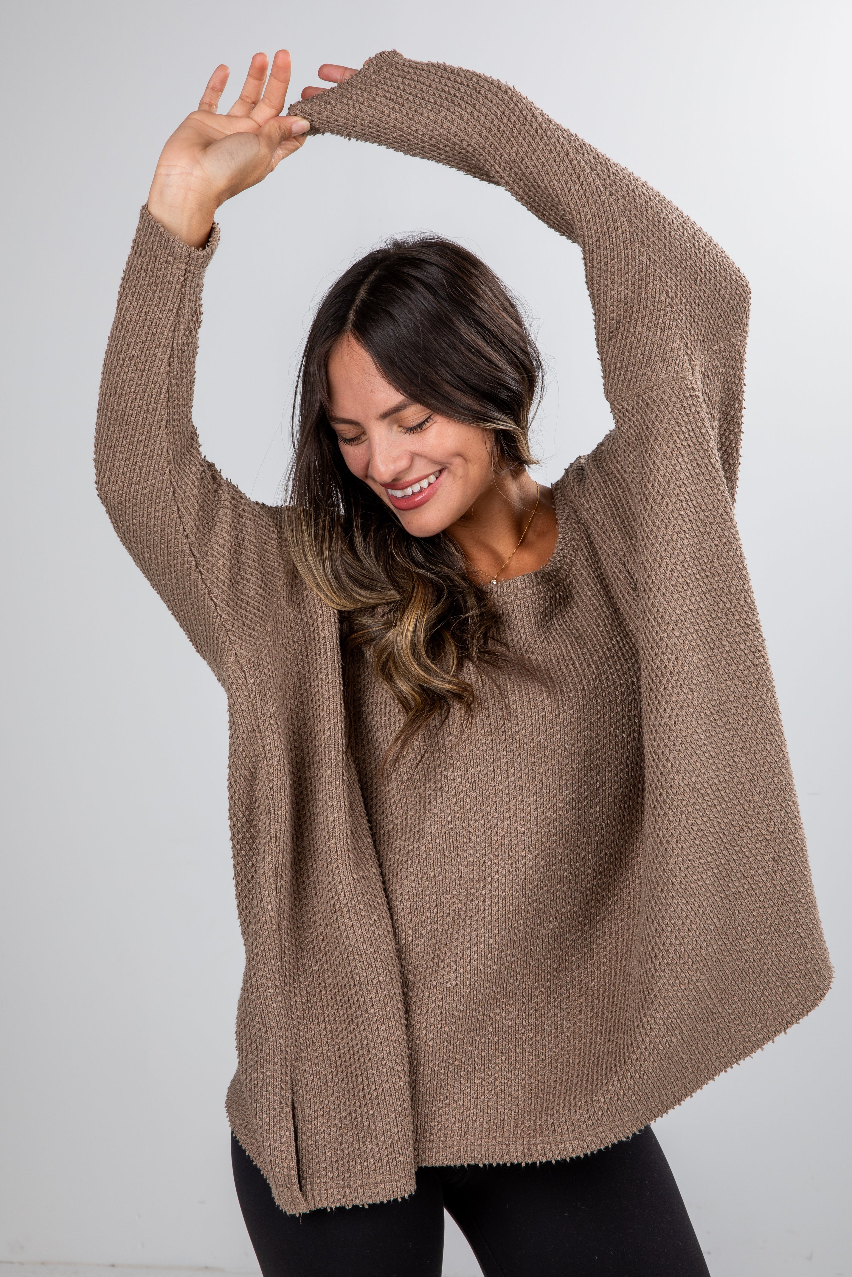 Woman wearing a brown sweater stretching her arms against a white background