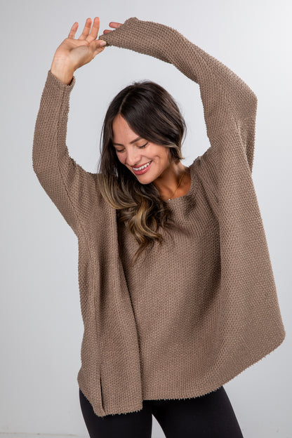 Woman wearing a brown sweater stretching her arms against a white background