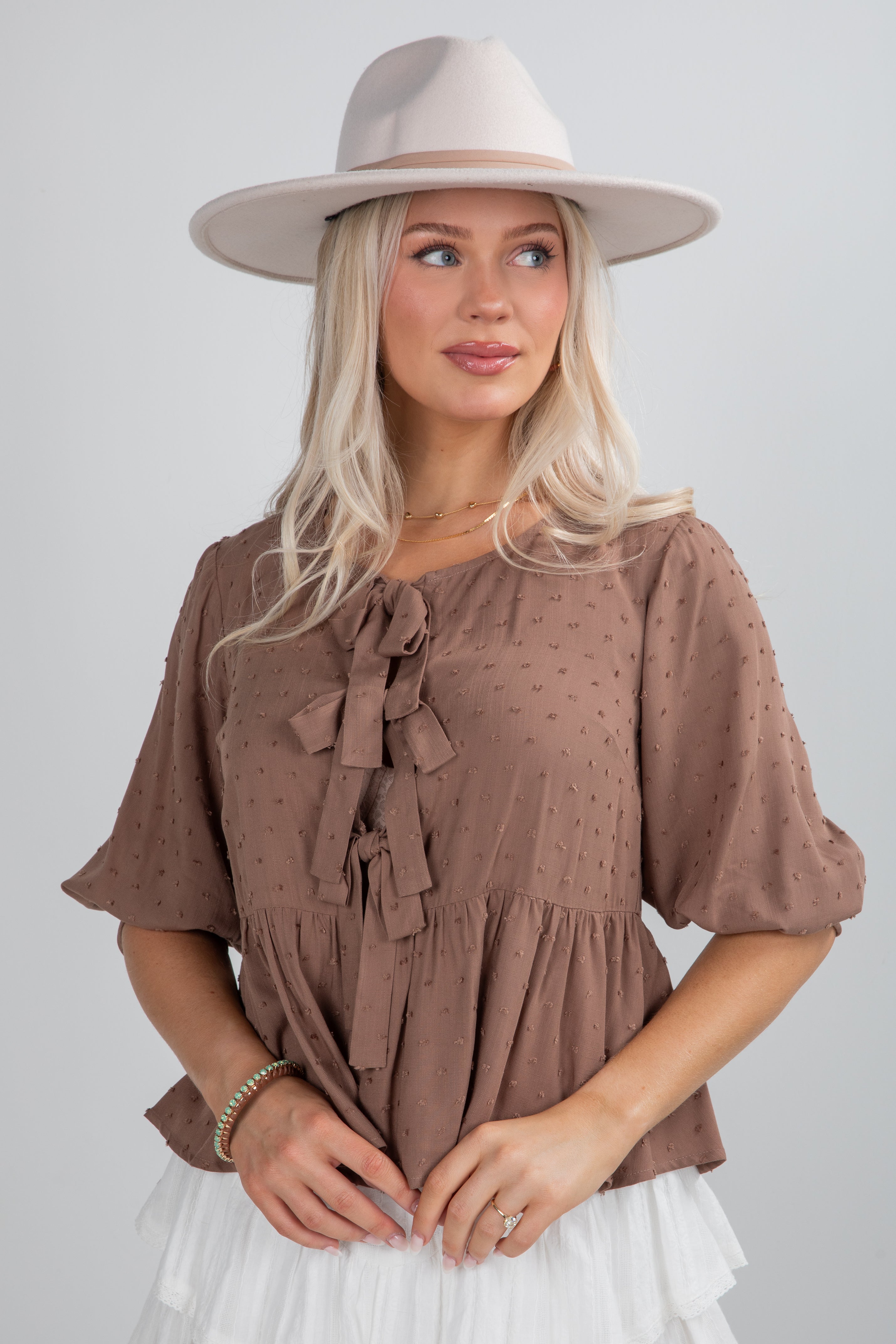 Woman wearing a brown blouse with ruffles and a beige hat on a plain background