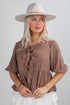 Woman wearing a brown blouse with ruffles and a beige hat on a plain background