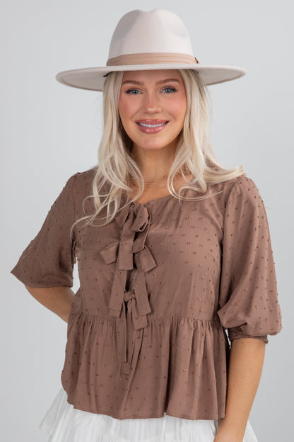 Woman wearing a brown blouse with puff sleeves and a beige hat on a white background