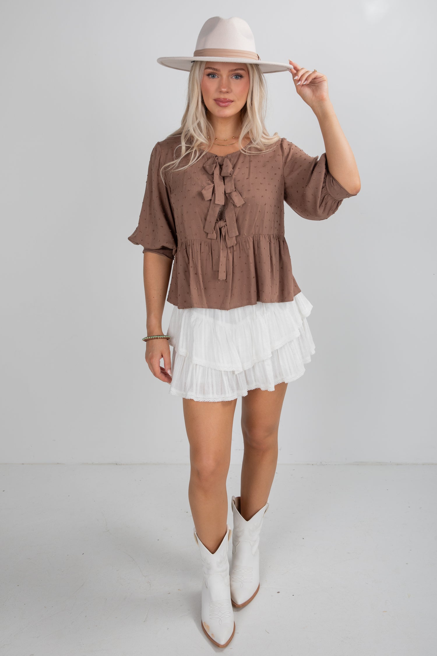 Woman wearing a brown blouse, white skirt, and white boots on a plain background