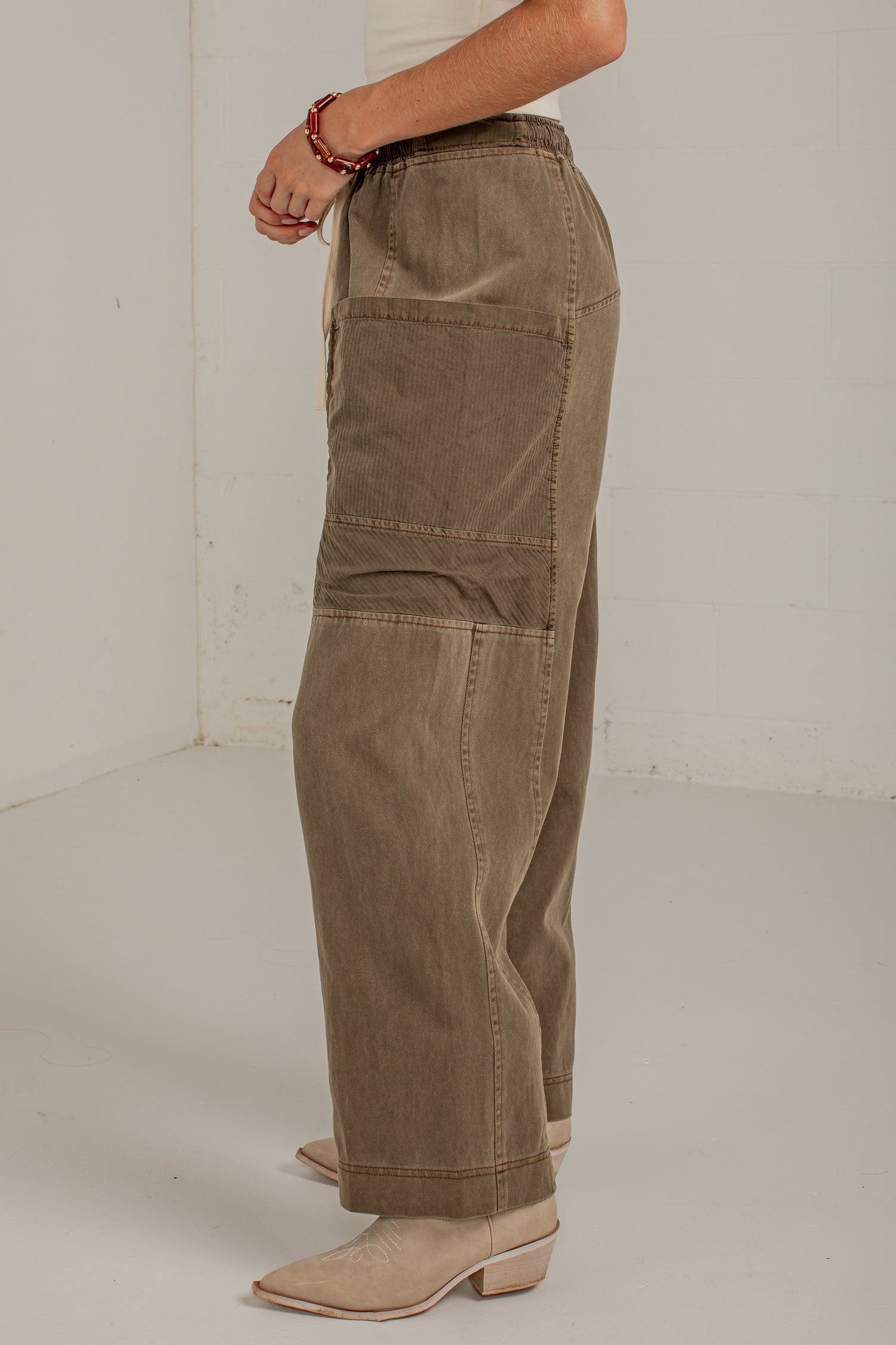 A person wearing wide-leg cargo-style pants in a taupe-brown corduroy fabric, paired with beige pointed-toe heeled mules, shown from the waist down in a studio setting.