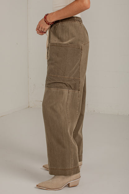 A person wearing wide-leg cargo-style pants in a taupe-brown corduroy fabric, paired with beige pointed-toe heeled mules, shown from the waist down in a studio setting.