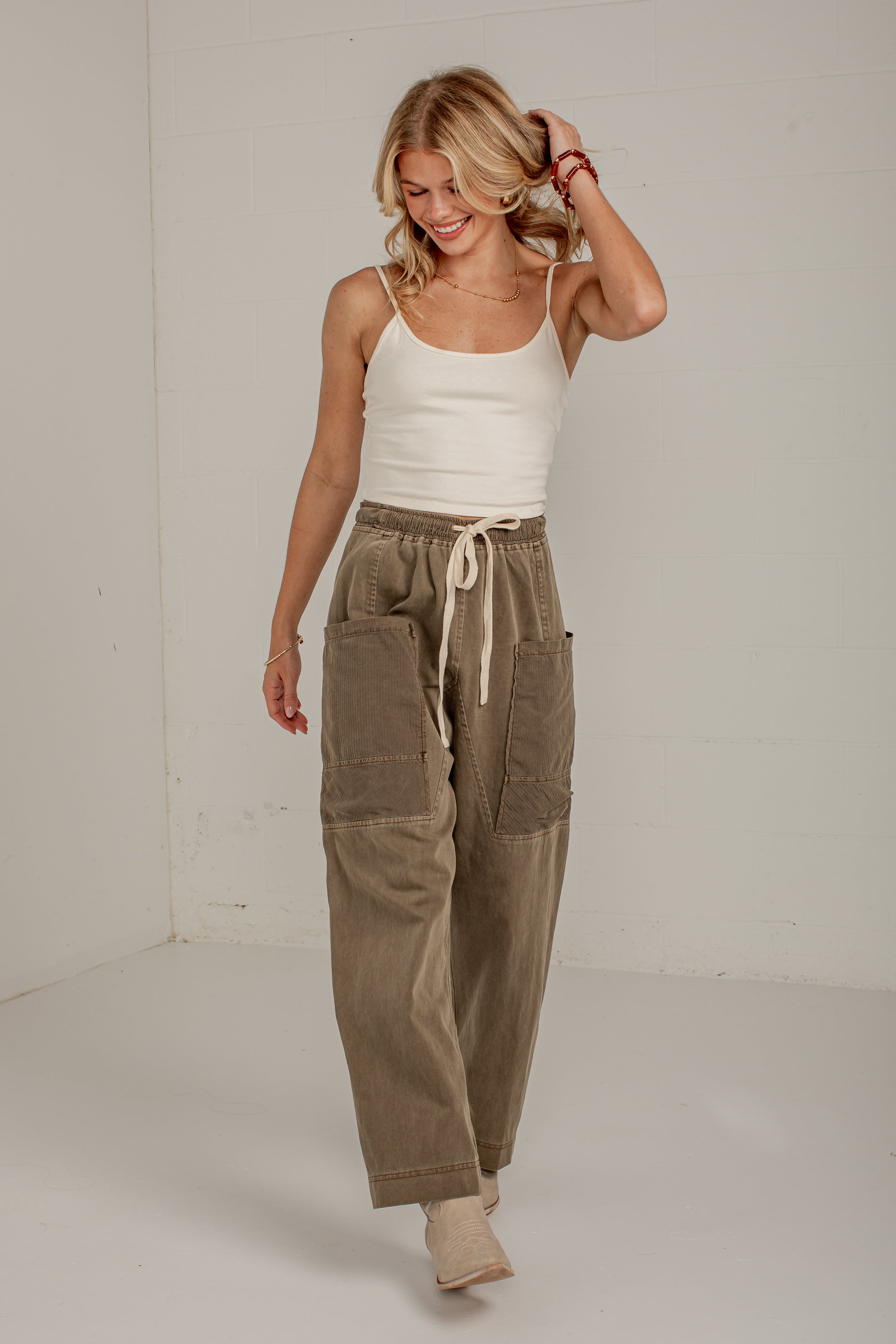 A woman modeling a pair of wide-leg, relaxed-fit corduroy pants in a warm taupe-brown color. The pants feature a drawstring waist, large patch pockets on the thighs, and a relaxed, comfortable fit.
