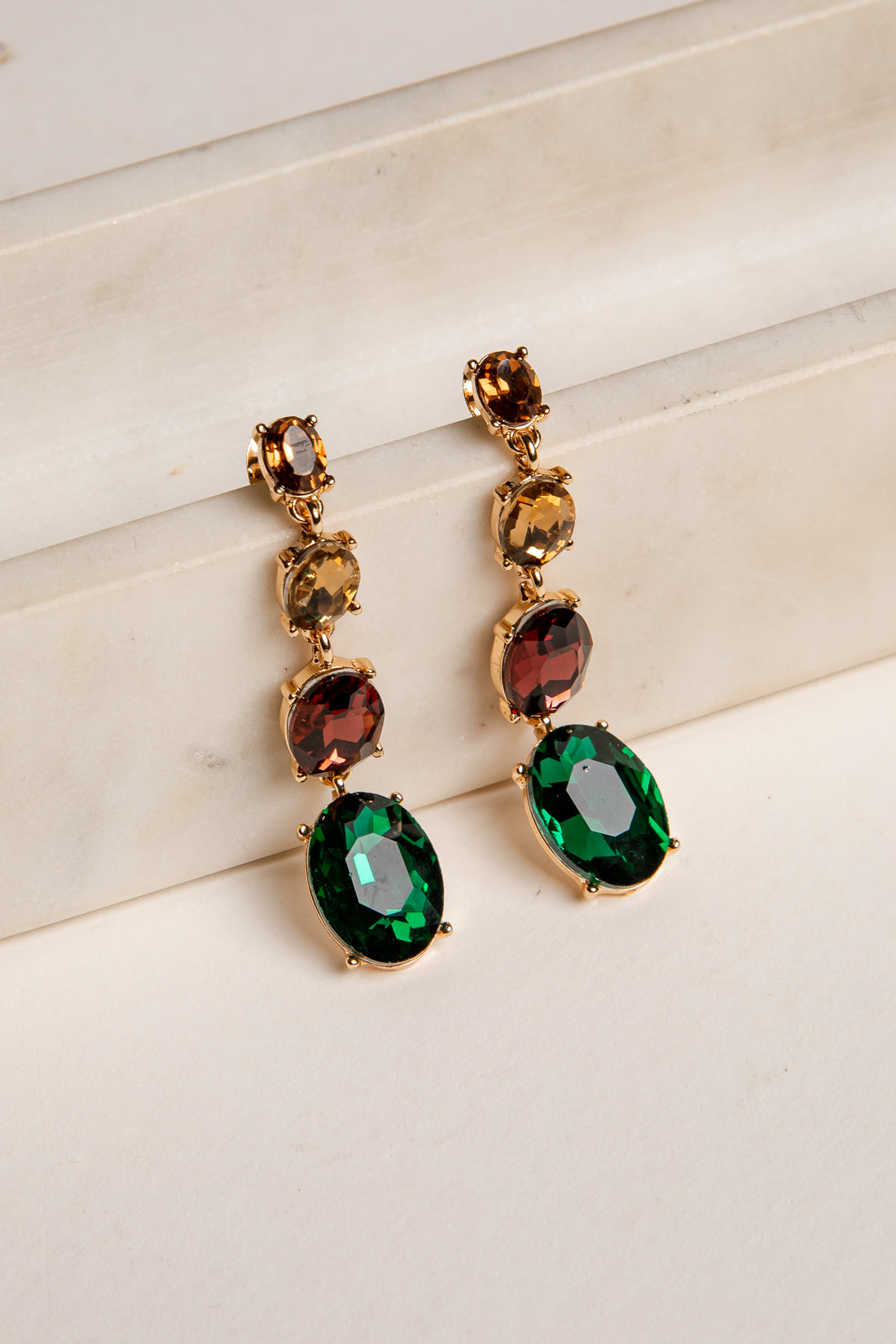 Gold earrings with green gemstones on a white surface