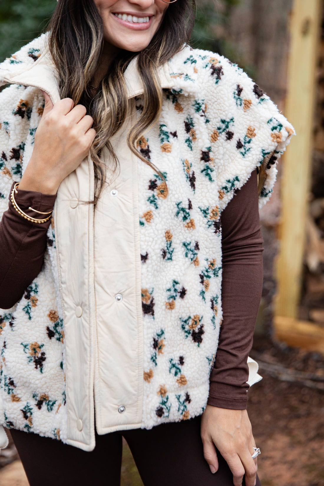 Person wearing a floral-patterned puffer vest over a brown long-sleeve shirt.