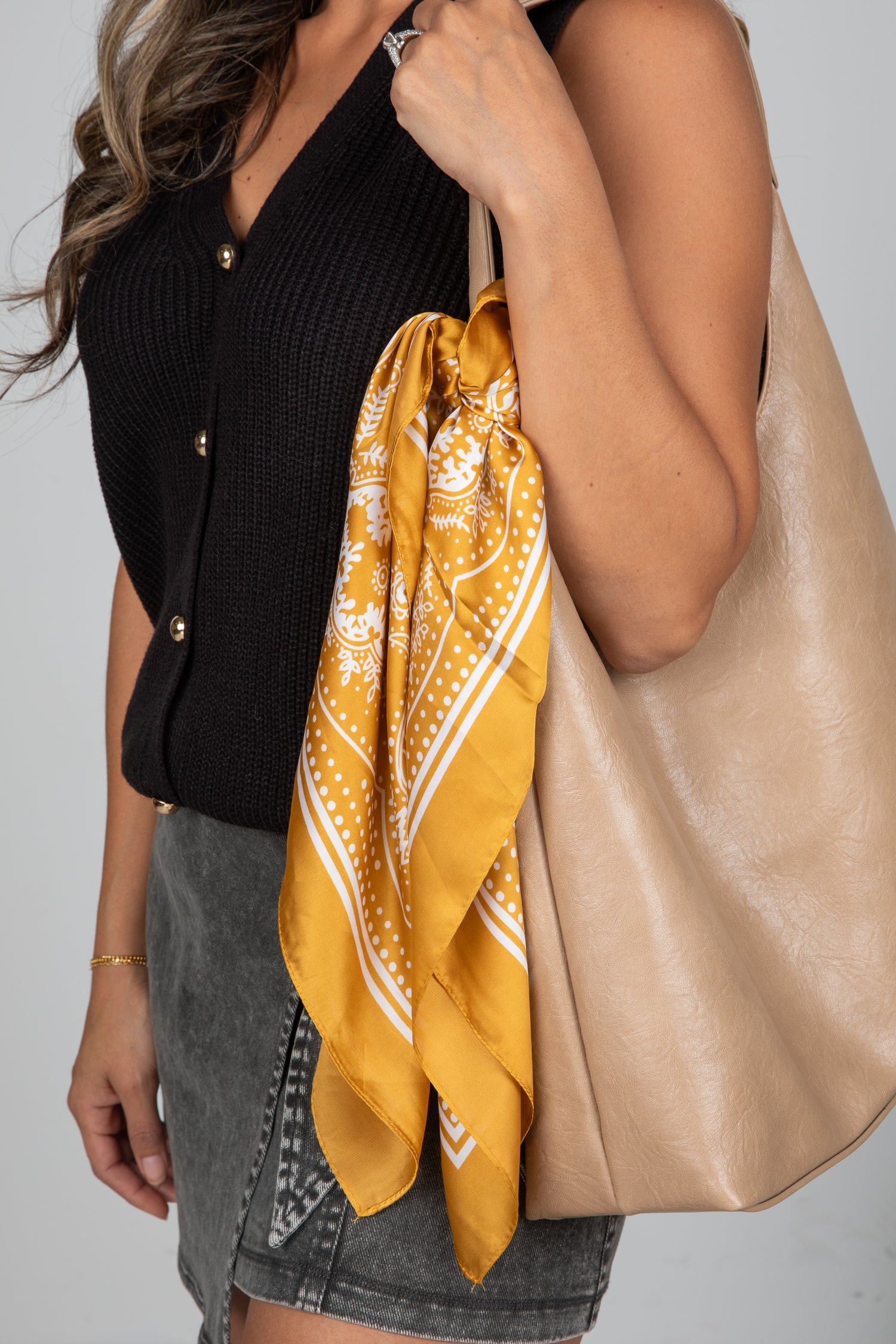 Person holding a beige tote bag with a yellow patterned scarf draped over it against a neutral background