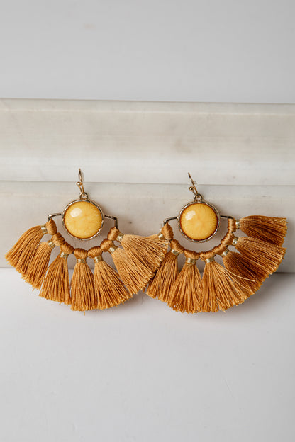 Pair of gold tassel earrings with yellow center on a light gray background