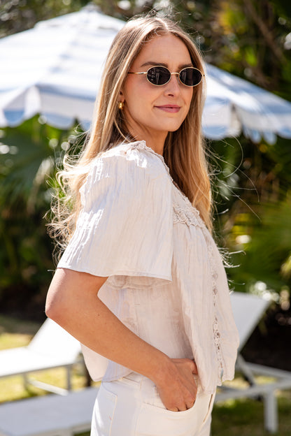 Woman wearing sunglasses and a light-colored outfit in an outdoor setting