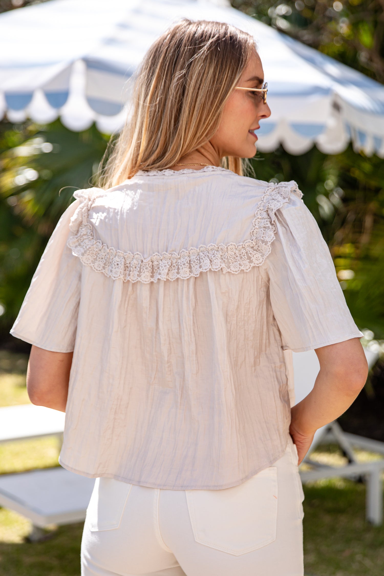 Woman wearing a light-colored blouse with lace details in an outdoor setting.
