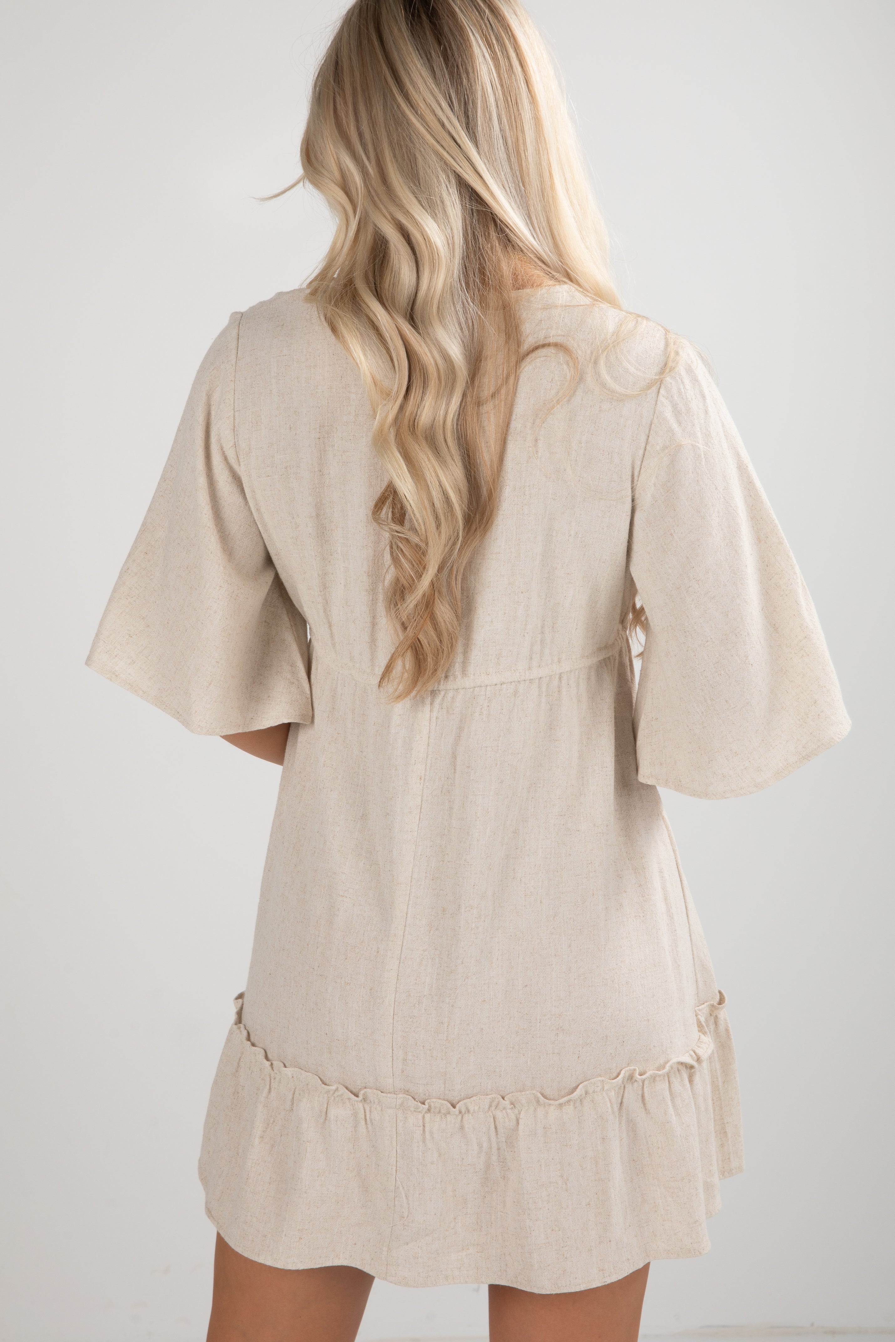 Beige dress with ruffled hem worn by a person with long blonde hair on a white background