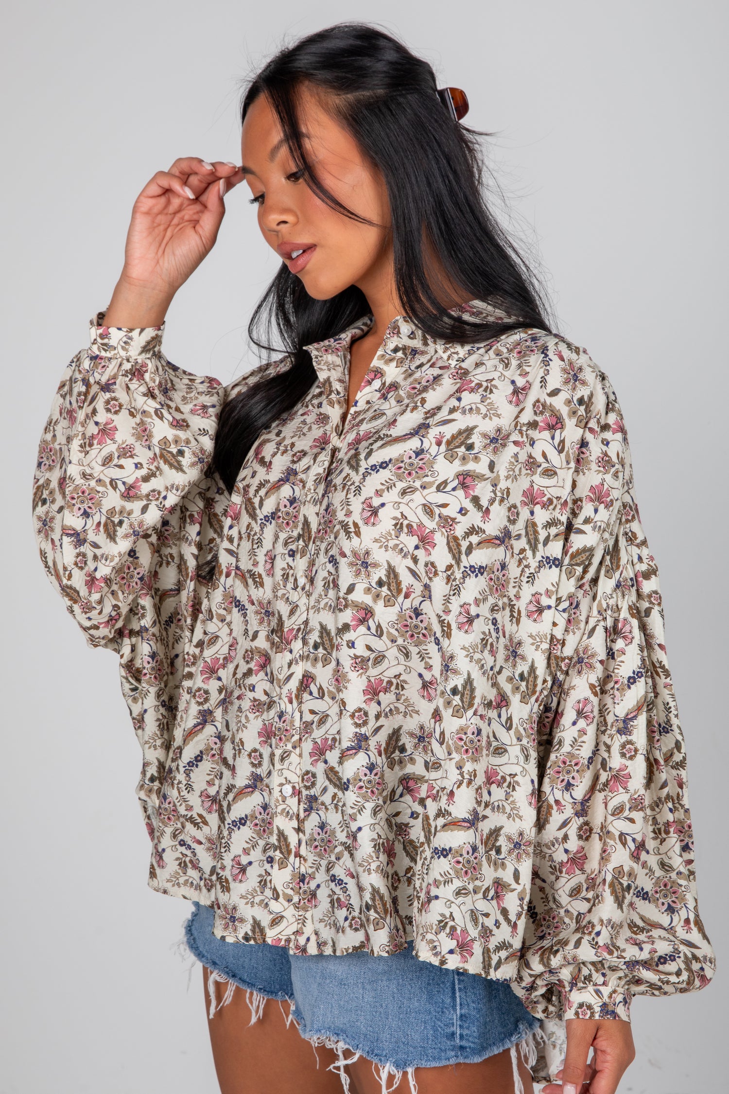 Woman wearing a floral blouse and denim shorts on a gray background