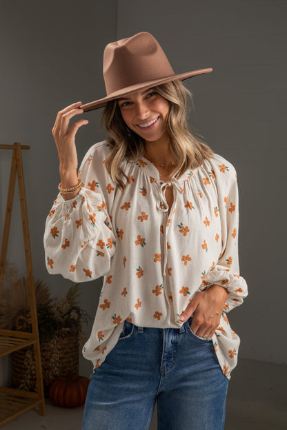 Woman wearing a floral blouse, jeans, and a brown hat indoors.