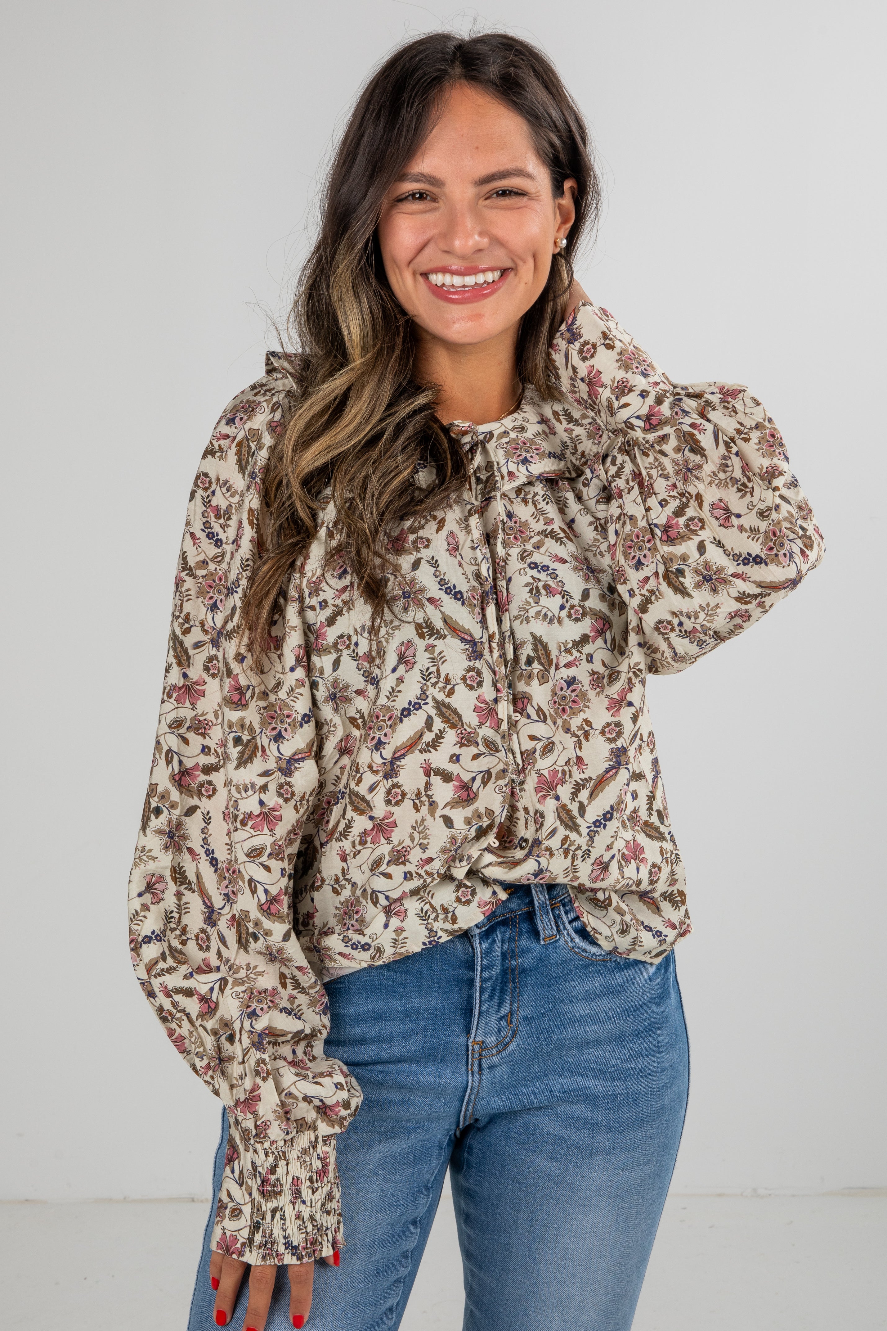 Woman wearing a floral blouse and blue jeans against a white background