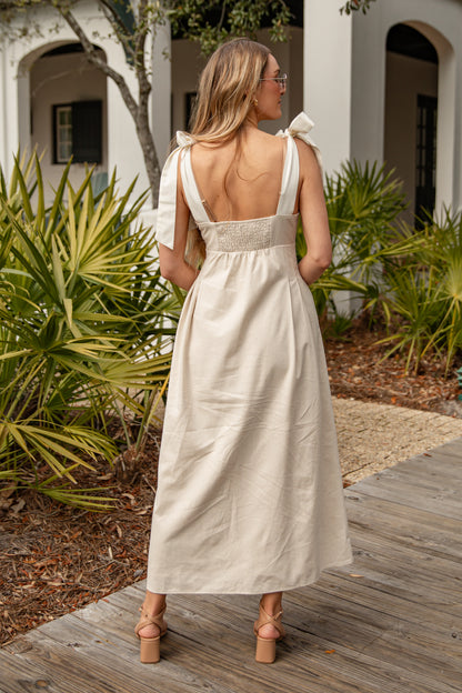 Woman in a white dress standing on a wooden deck with plants and a building in the background