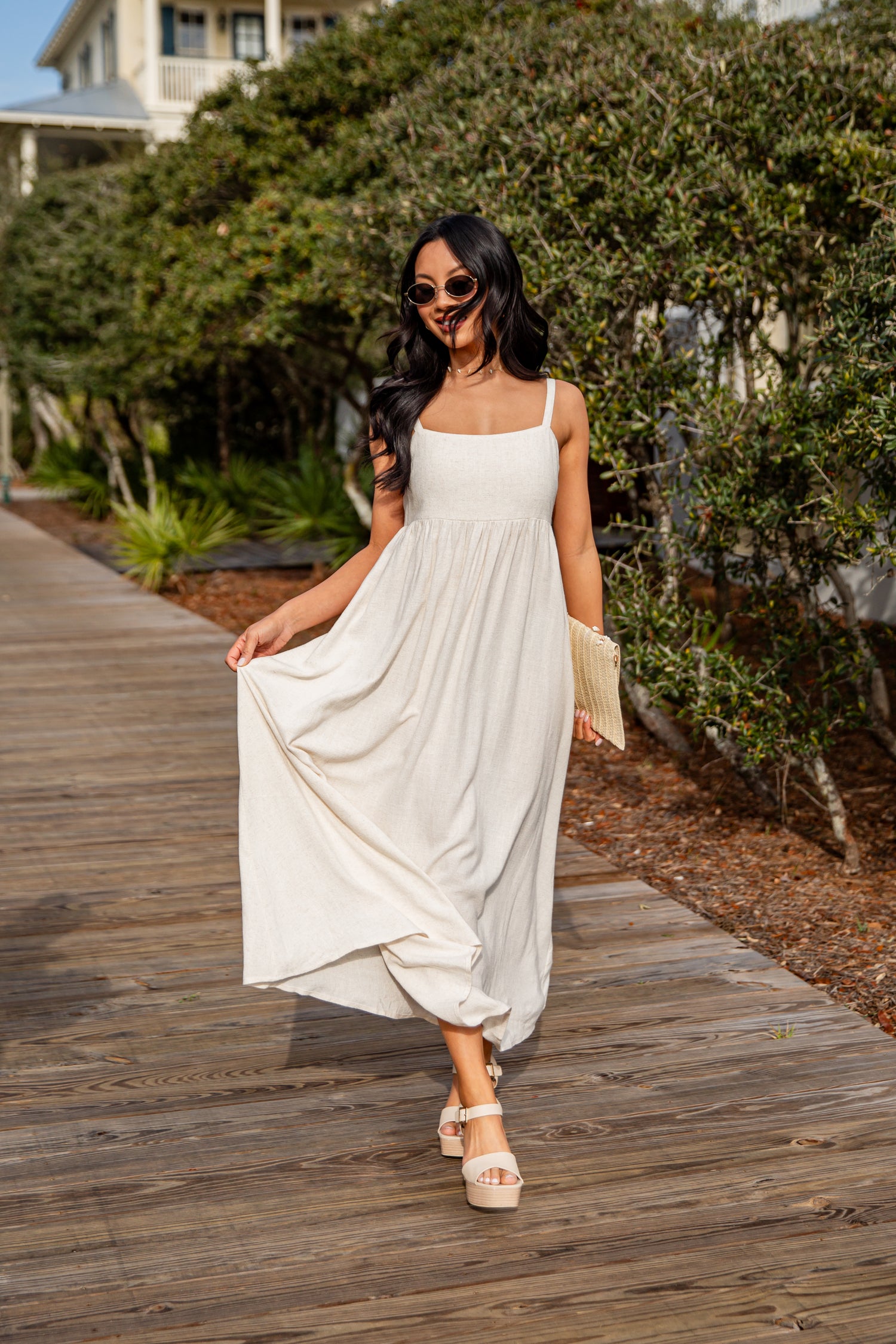 Woman in a white dress walking on a wooden boardwalk with greenery in the background