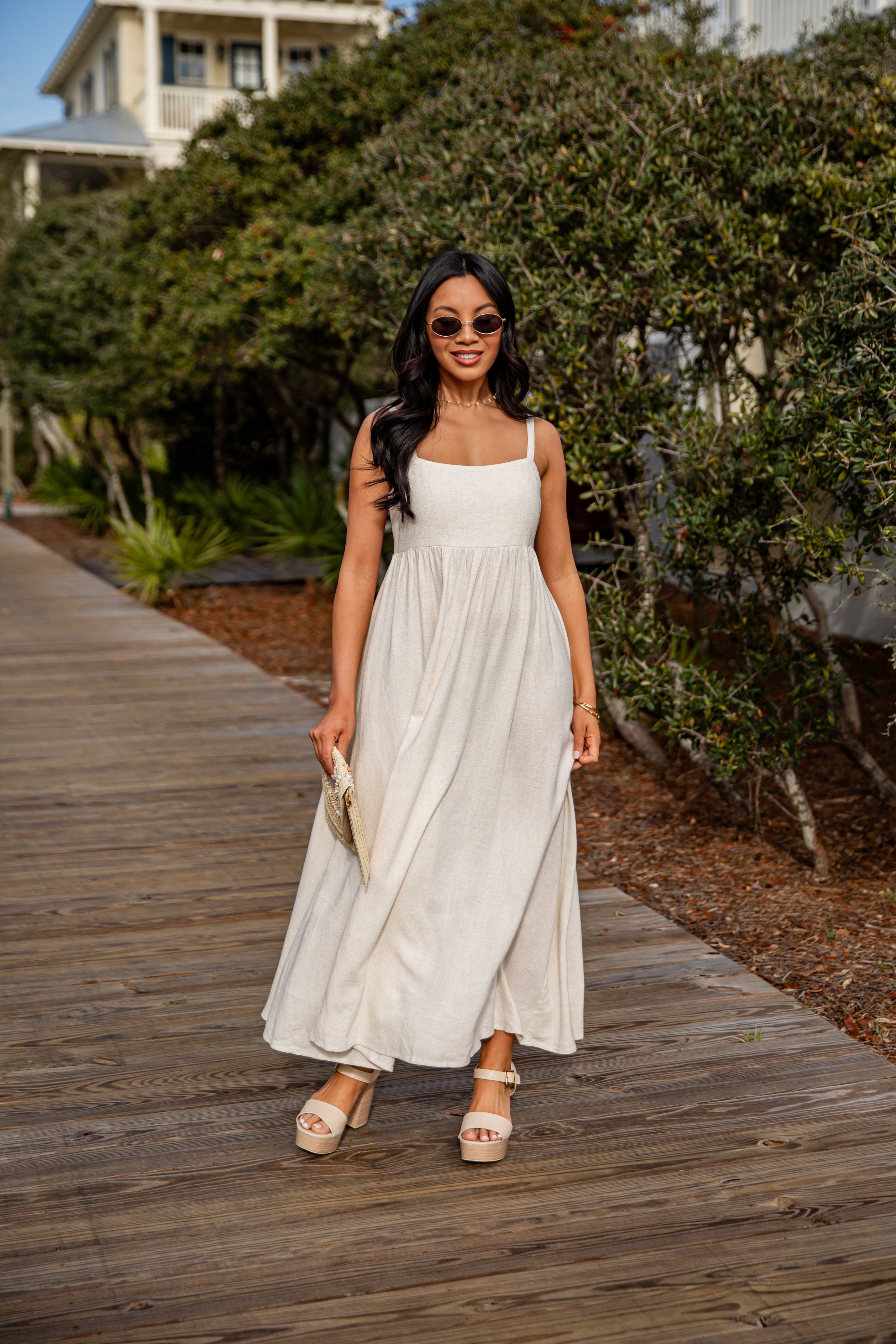 Woman in a white dress standing on a wooden boardwalk with greenery in the background