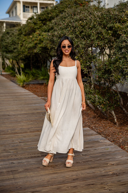 Woman in a white dress standing on a wooden boardwalk with greenery in the background