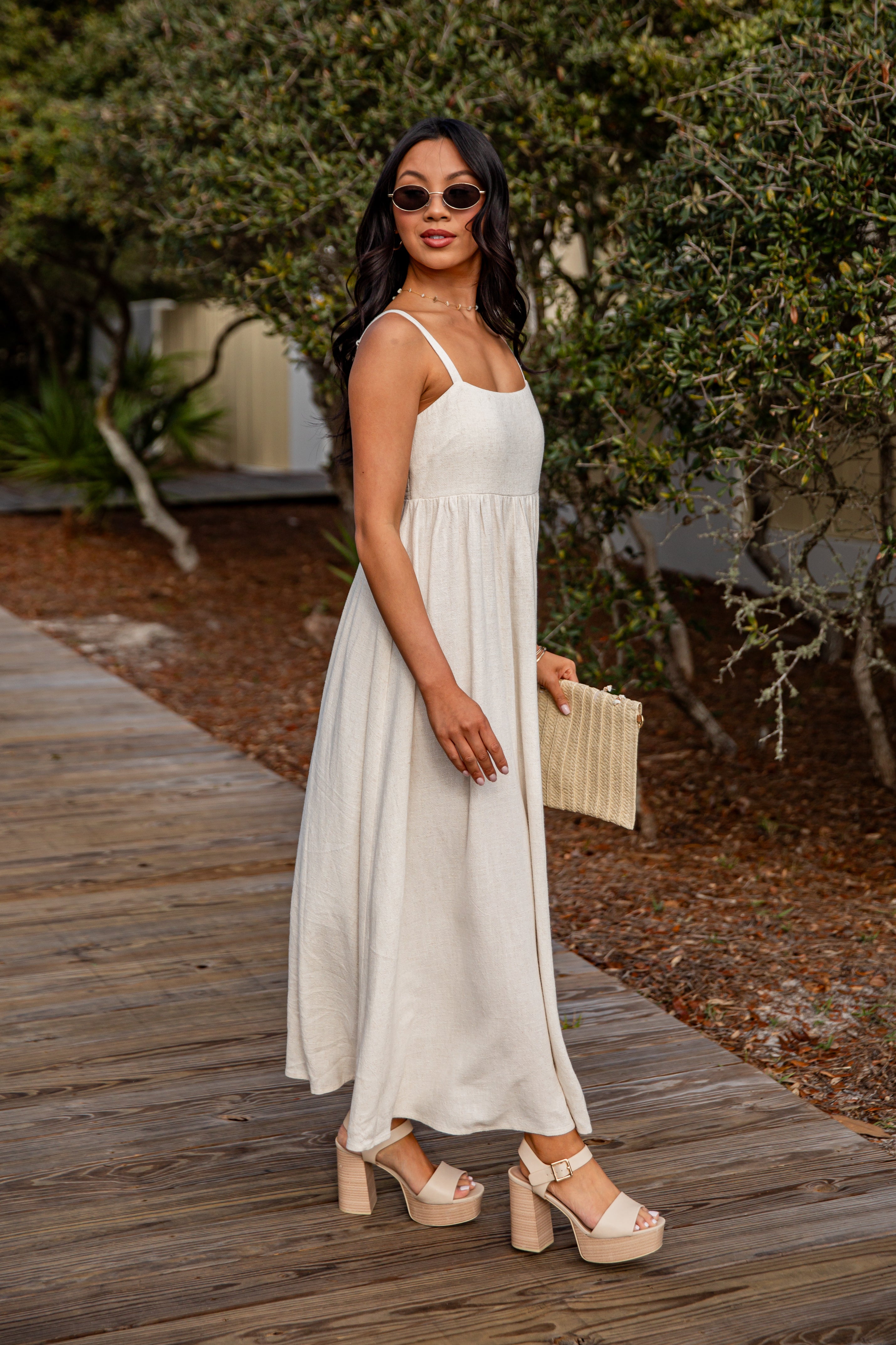 Woman in a white dress standing on a wooden path with greenery in the background