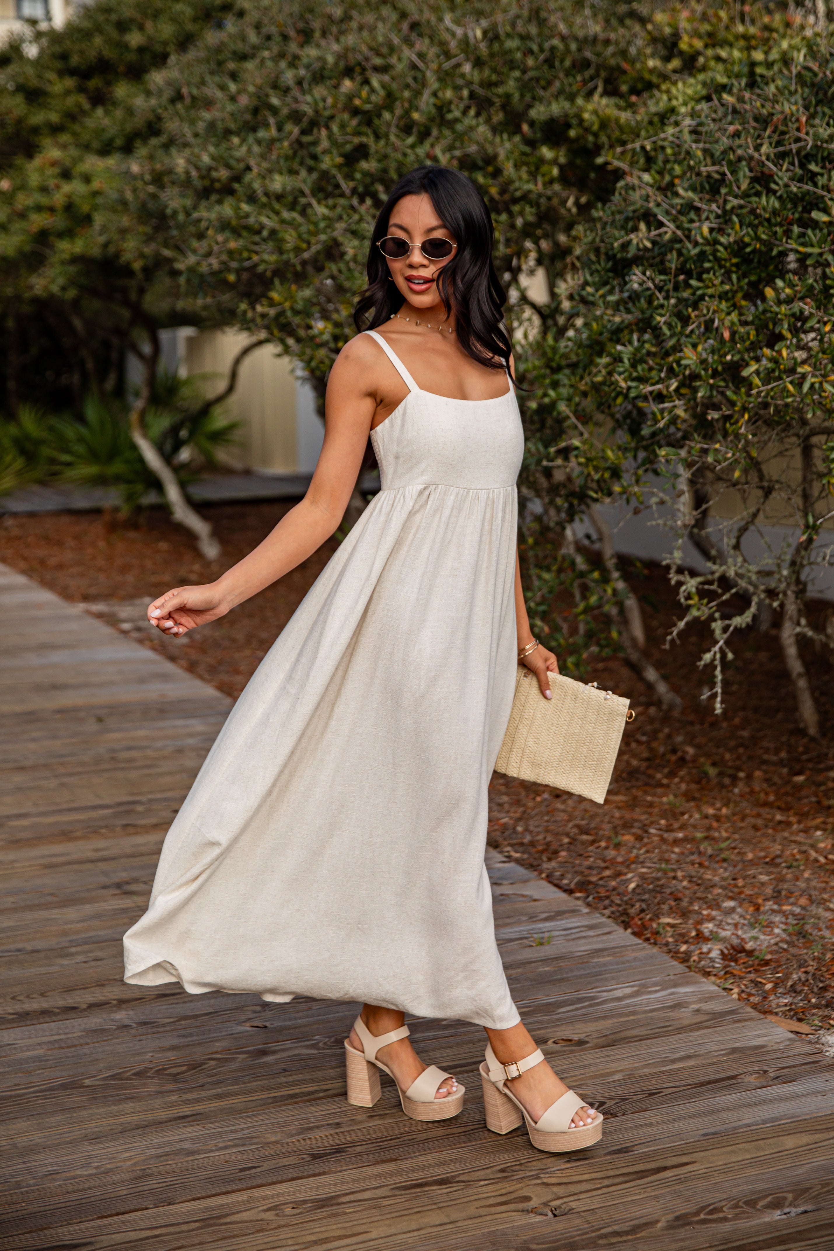 Woman in a white dress standing on a wooden path with greenery in the background