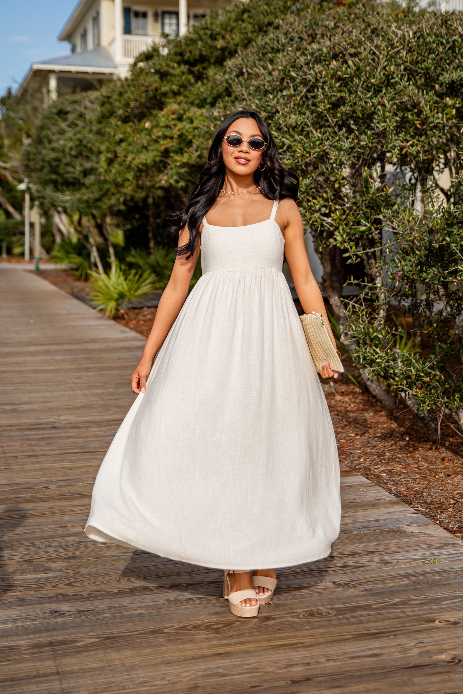 Woman in a white dress walking on a wooden boardwalk with greenery in the background