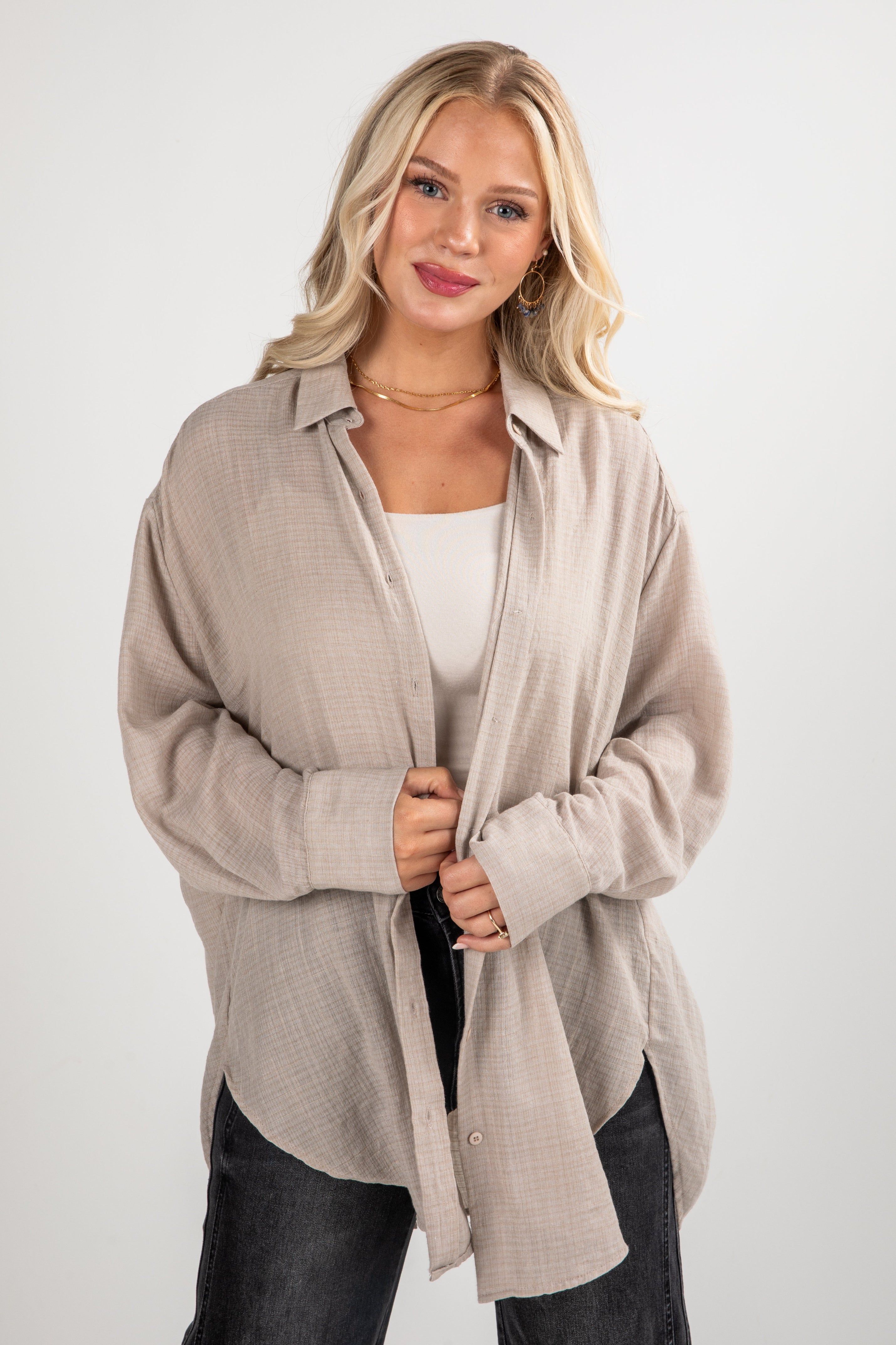 Woman wearing a beige cardigan over a white top and black pants on a white background