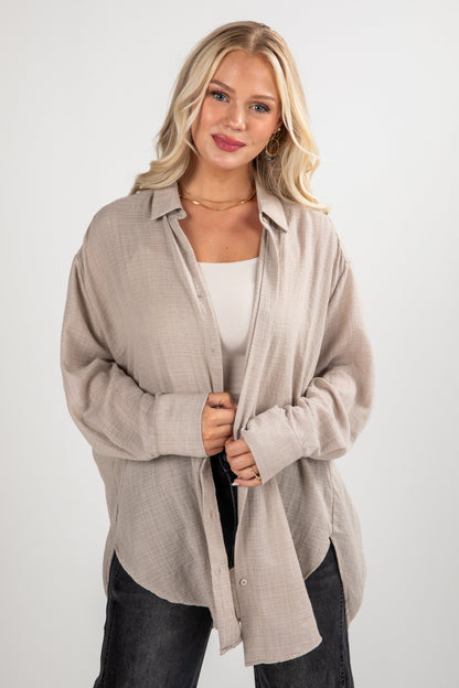 Woman wearing a beige cardigan over a white top and black pants on a white background