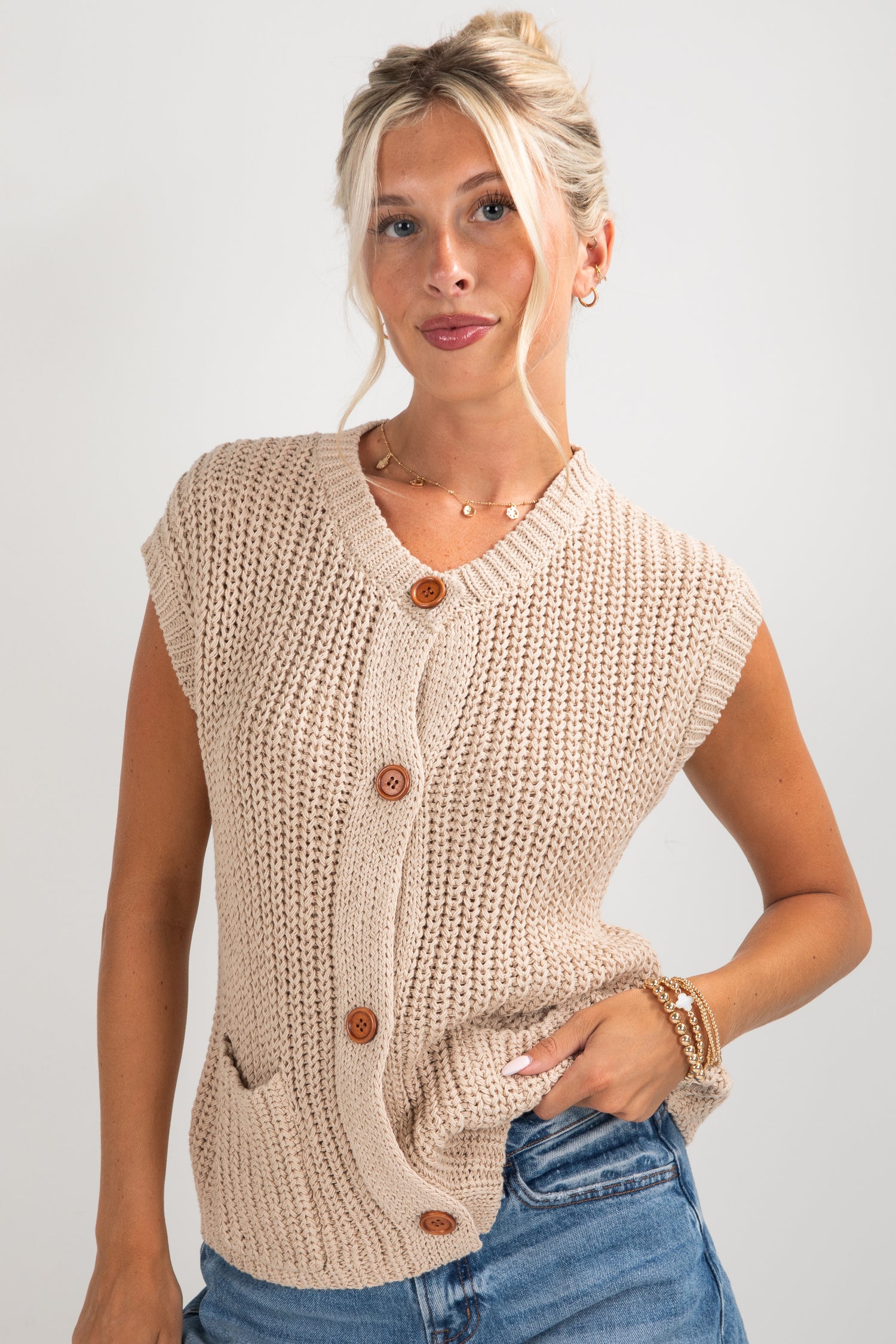 Woman wearing a beige knitted vest with buttons on a plain background