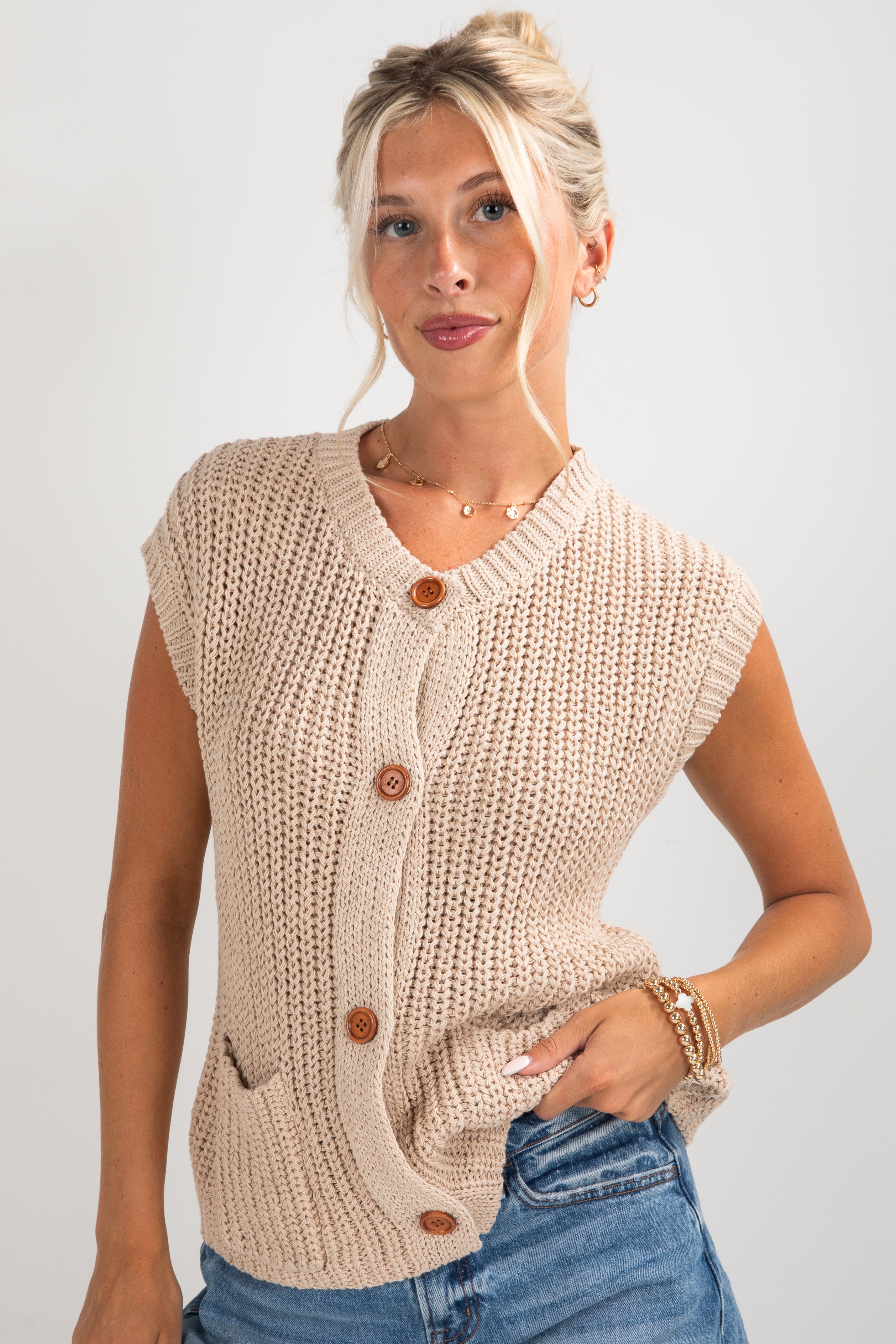Woman wearing a beige knitted vest with buttons on a plain background